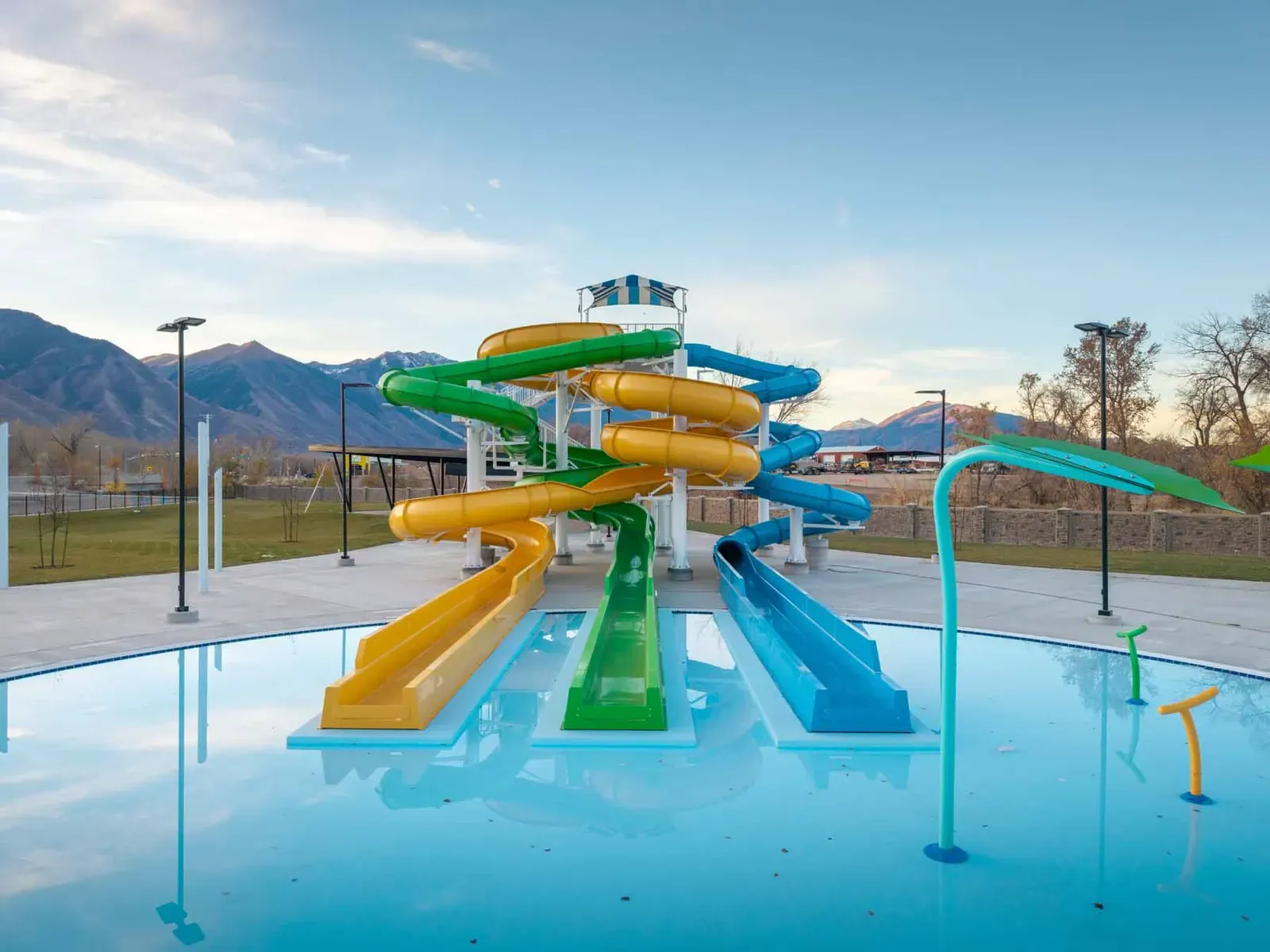 Outdoor pool with yellow, green and blue water slides and spray features, with mountains in the background.