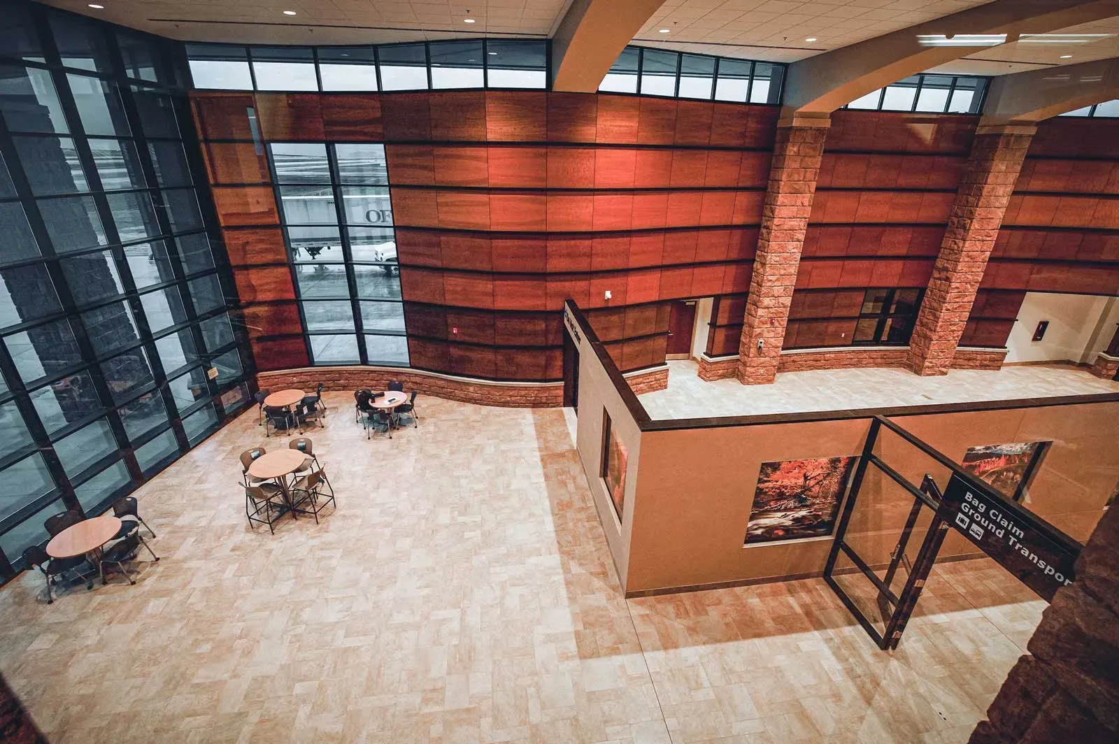 Elevated view of the terminal atrium with round tables, wood panel walls and stone columns, and a ground transportation sign at right.