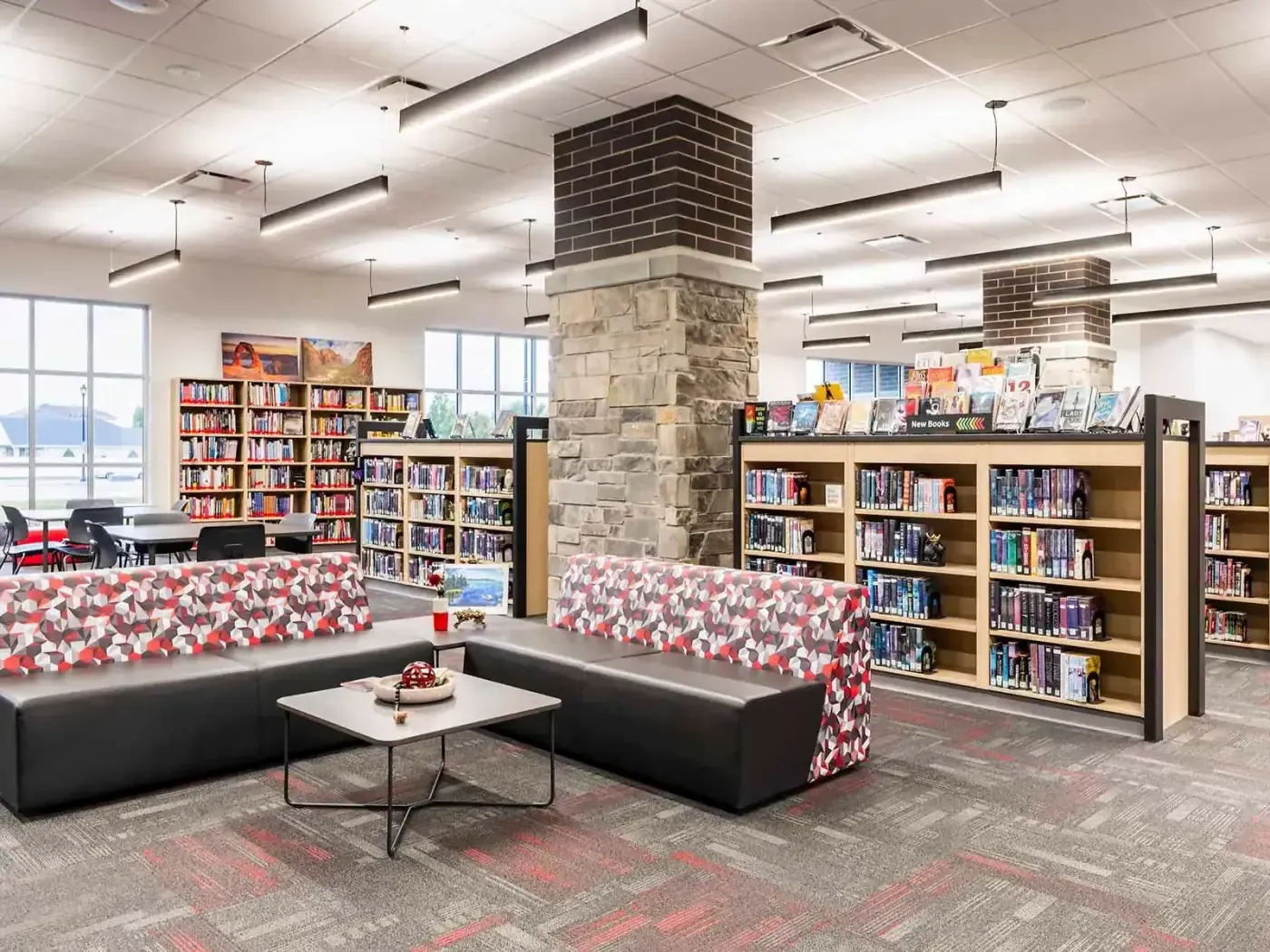 Media center with low bookshelves, red-patterned lounge seating, and a stone-and-brick column.