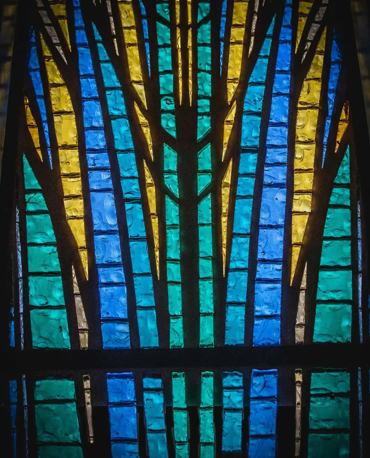 Close-up of a blue, green, and gold stained glass window with a vertical tree-like pattern