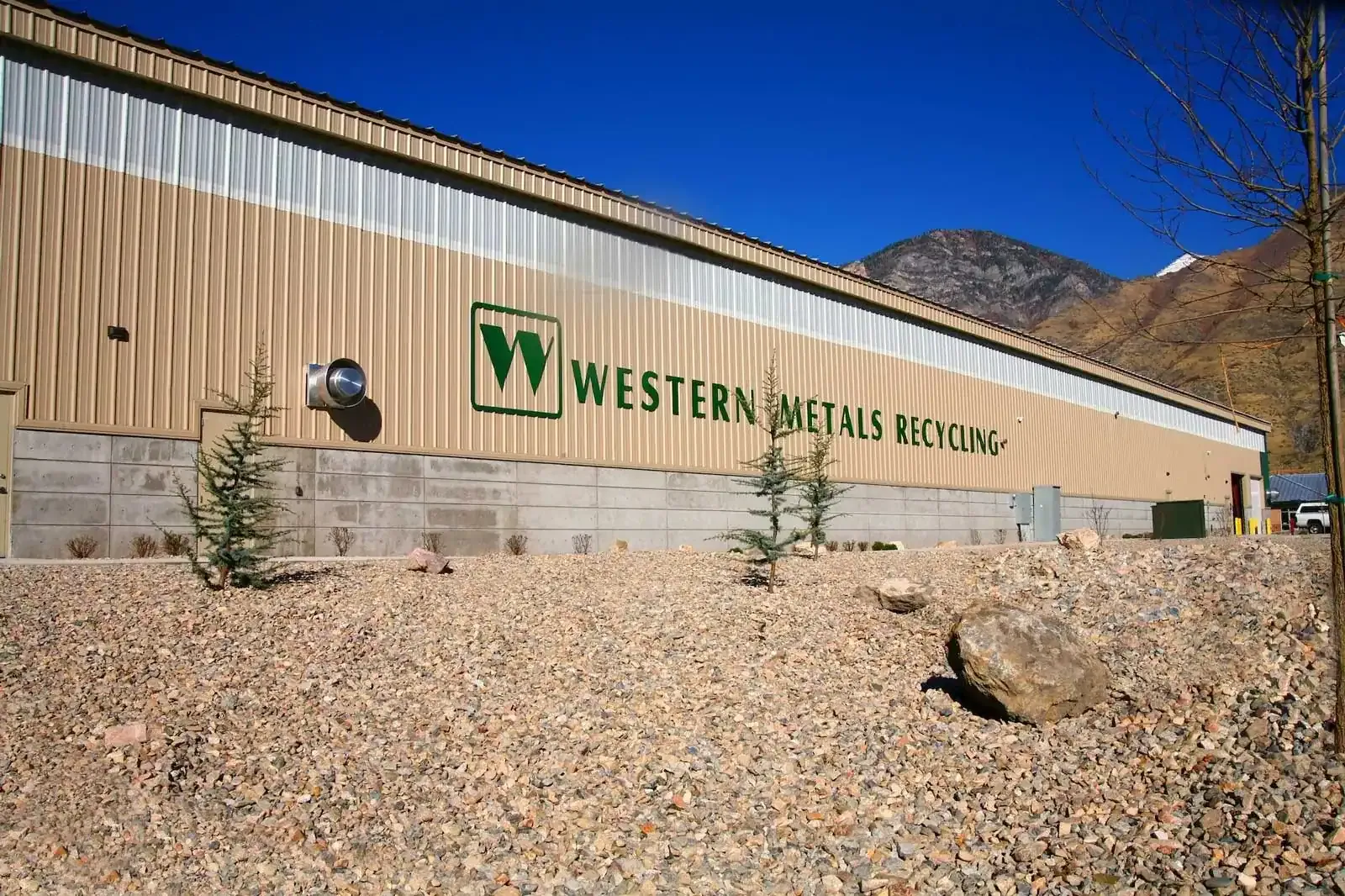 Western Metals Recycling logo on a tan metal wall above a concrete base, with rock landscaping in front.