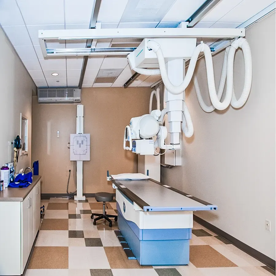 Second x-ray room with a ceiling-mounted unit, a wall stand and a table on a checkered tile floor