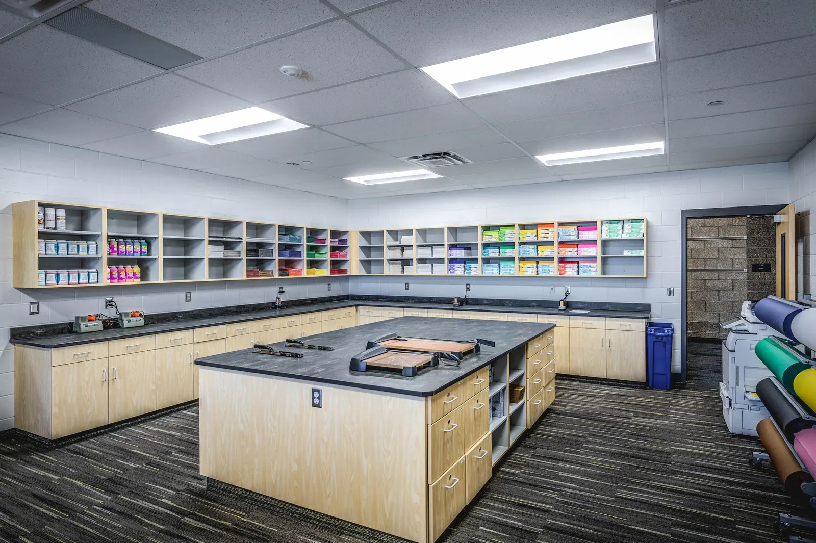 Teacher workroom with an island worktable, supply shelving and rolls of colored paper