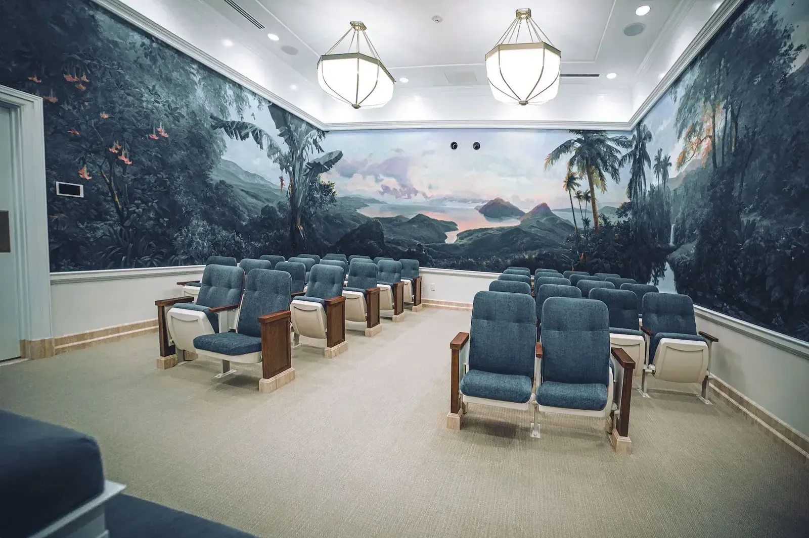 Room with a hand-painted tropical island mural across the walls and rows of blue upholstered chairs.