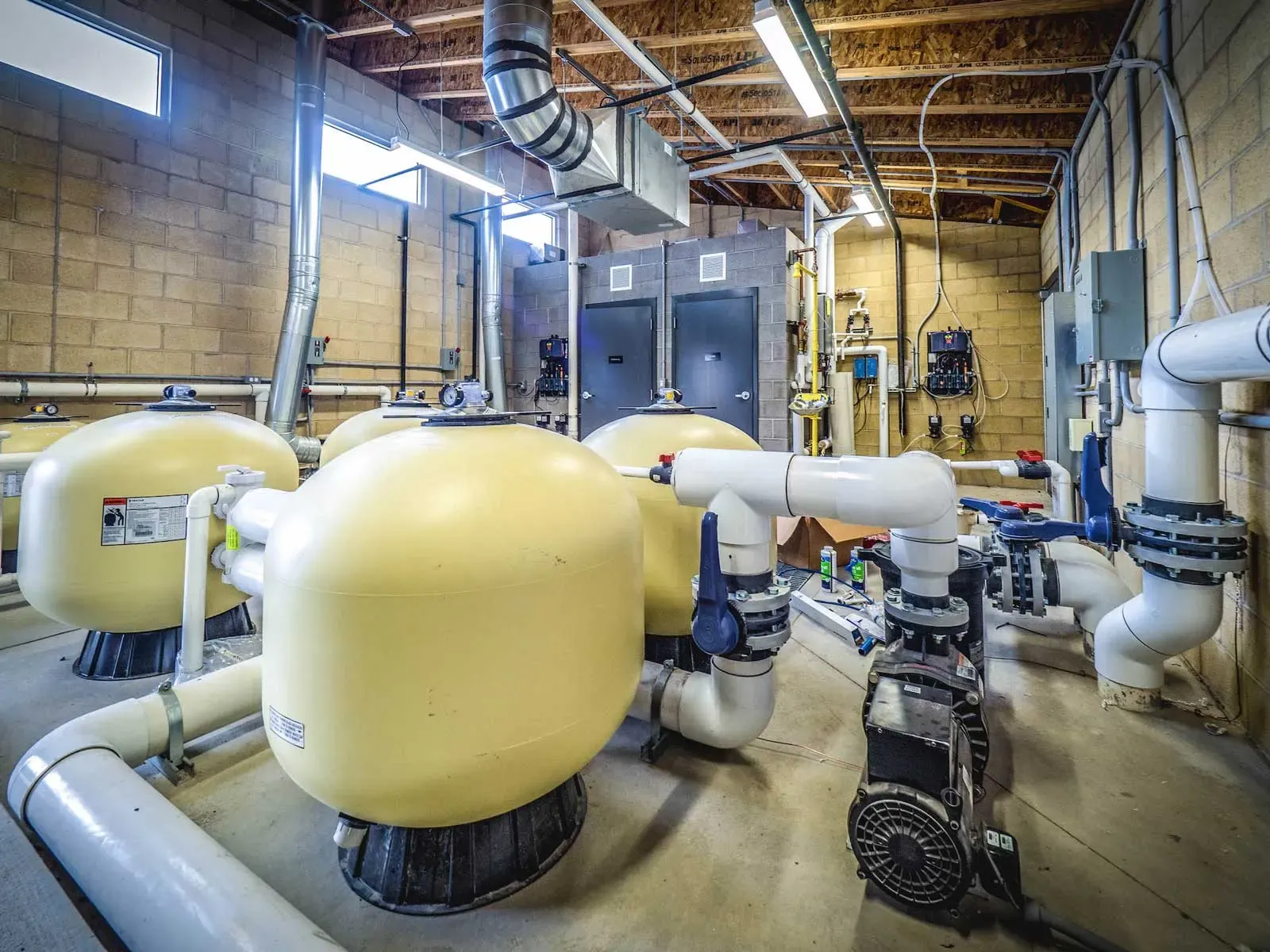 Pool equipment room with yellow filter tanks, pumps and piping.