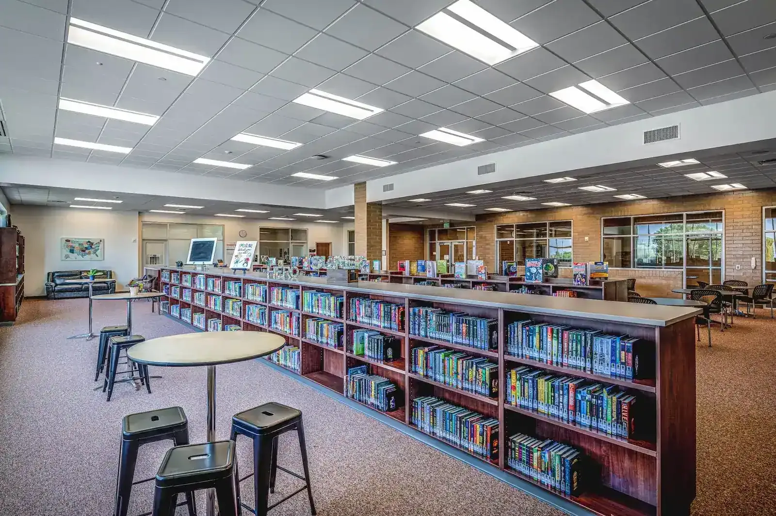Library with wood bookshelves, high-top tables and stools under a gridded ceiling.