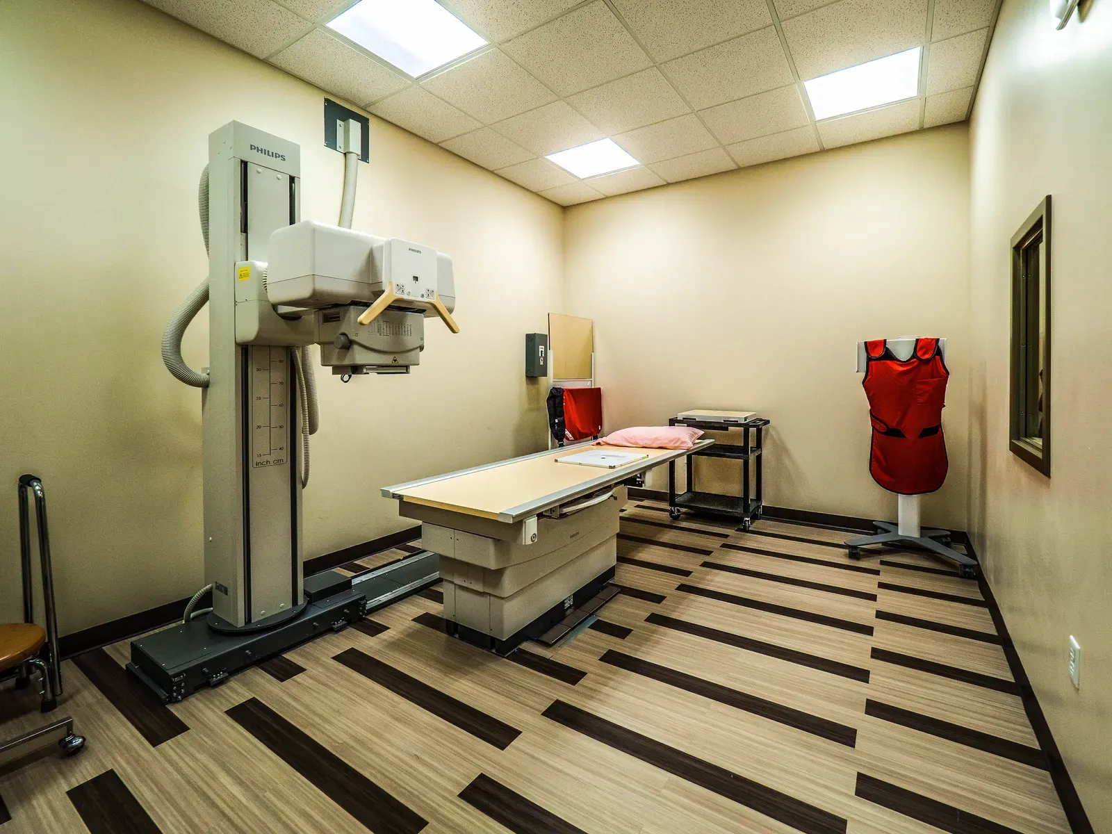 X-ray room with an x-ray machine, an exam table and a lead apron on a stand.