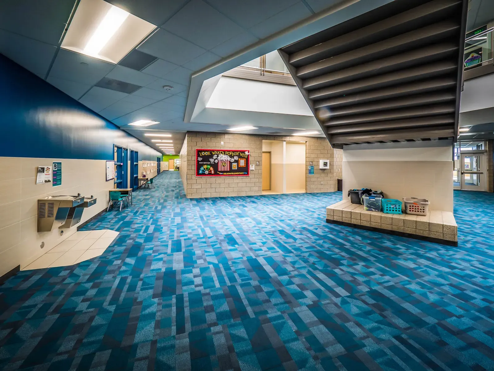 Open hallway with a drinking fountain, a built-in bench with baskets and a stairway overhead