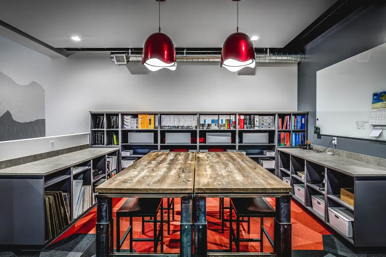 Materials library with a long wood work table, red pendant lights and open shelving