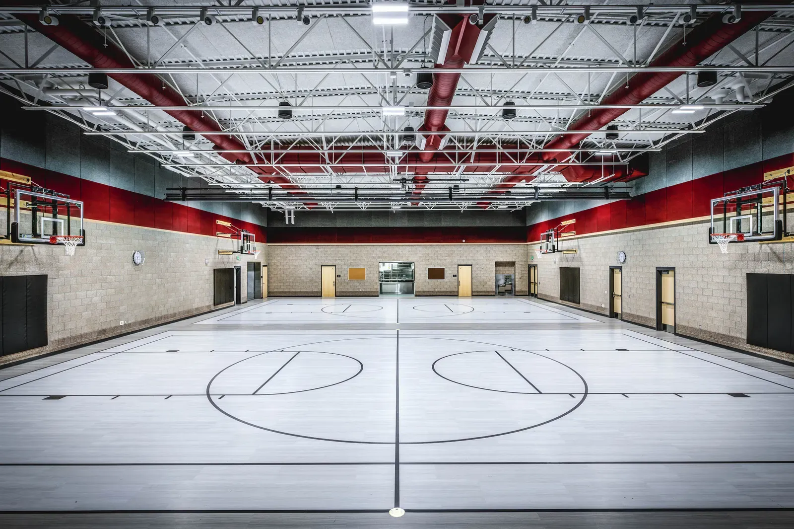 Gymnasium with a painted court floor, red steel roof trusses and wall-mounted basketball hoops
