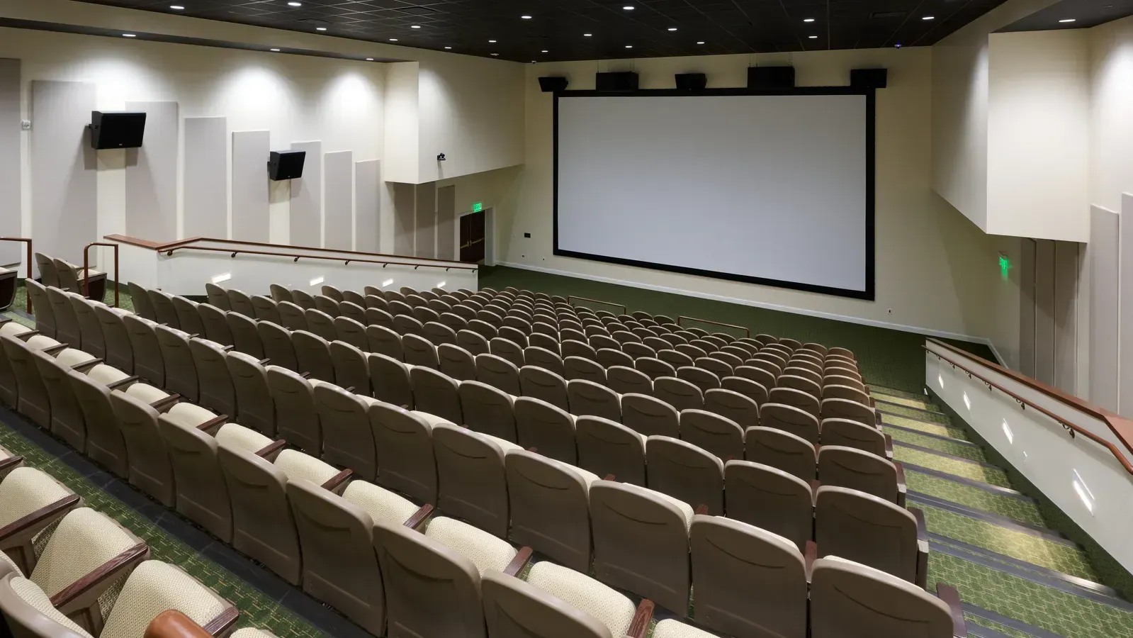 Tiered theater with rows of cushioned seats facing a large projection screen.