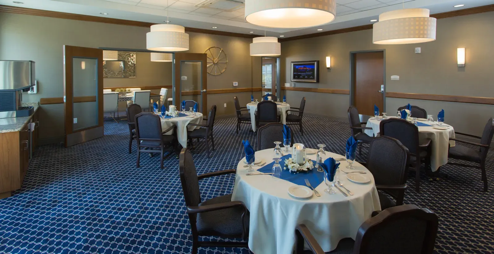 Dining room with round tables set with white cloths and blue napkins.