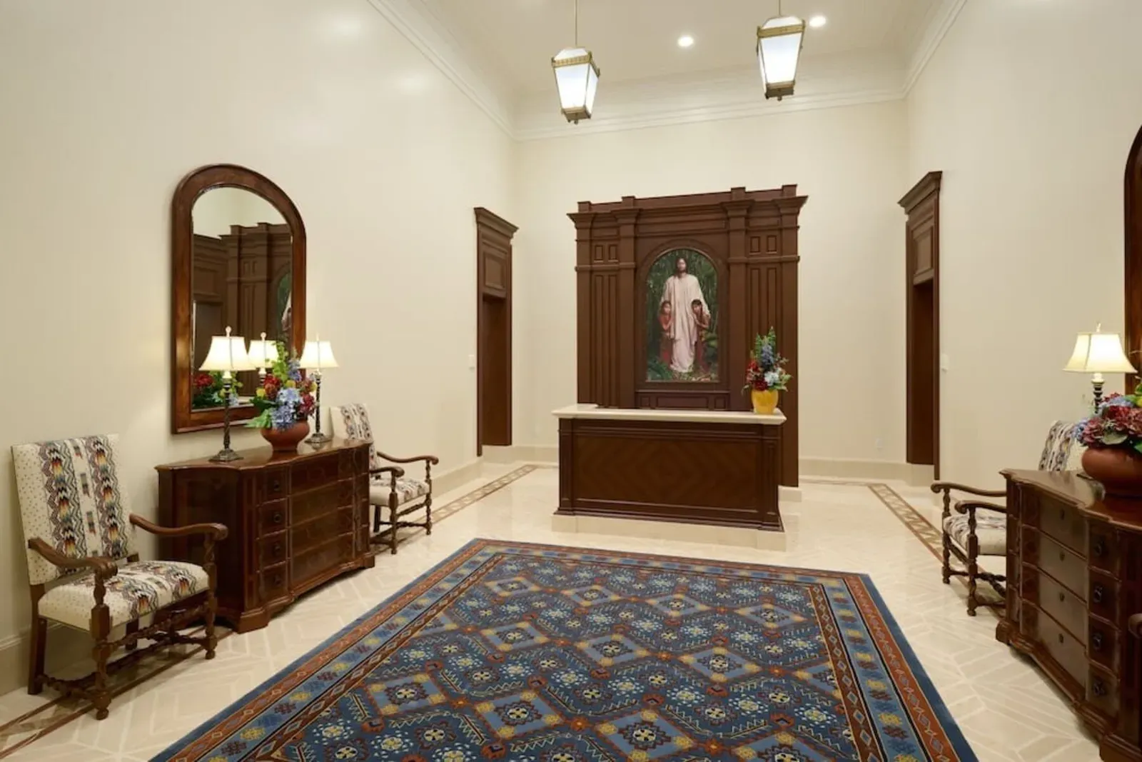 Entry area with a wood reception desk beneath a painting in a carved frame, a blue patterned rug, wood dressers and upholstered chairs