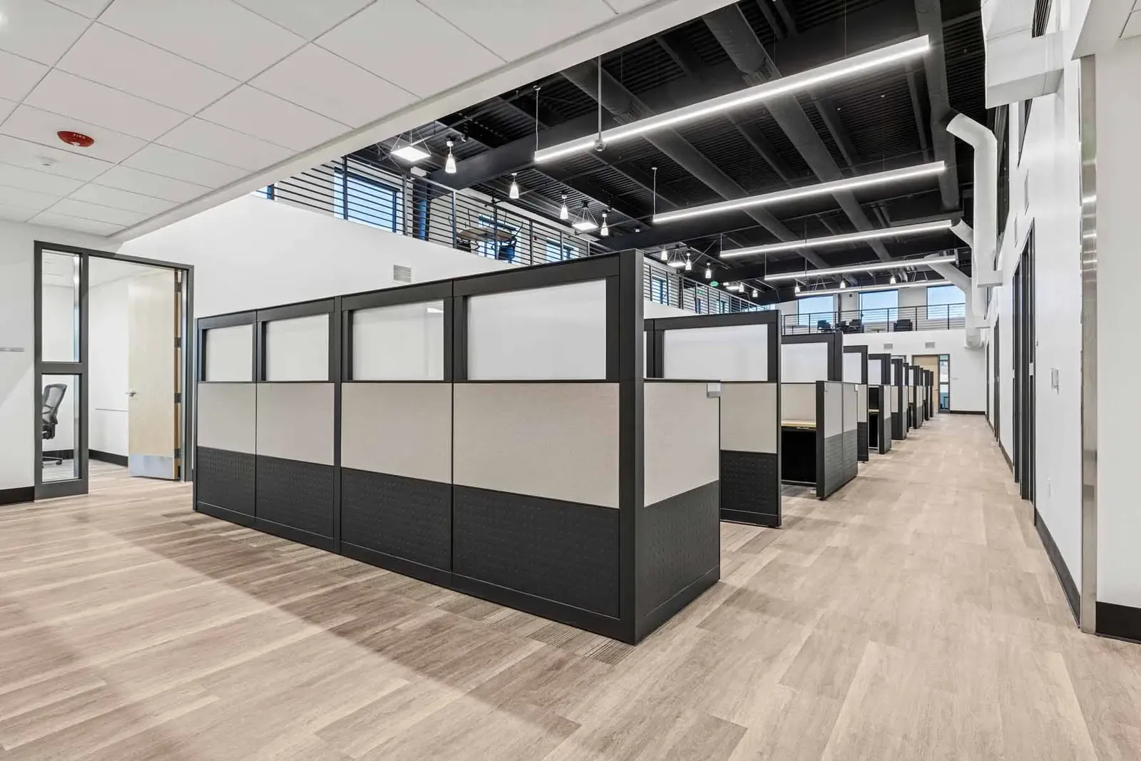 Rows of cubicle workstations with dark partitions along a wood-look floor.