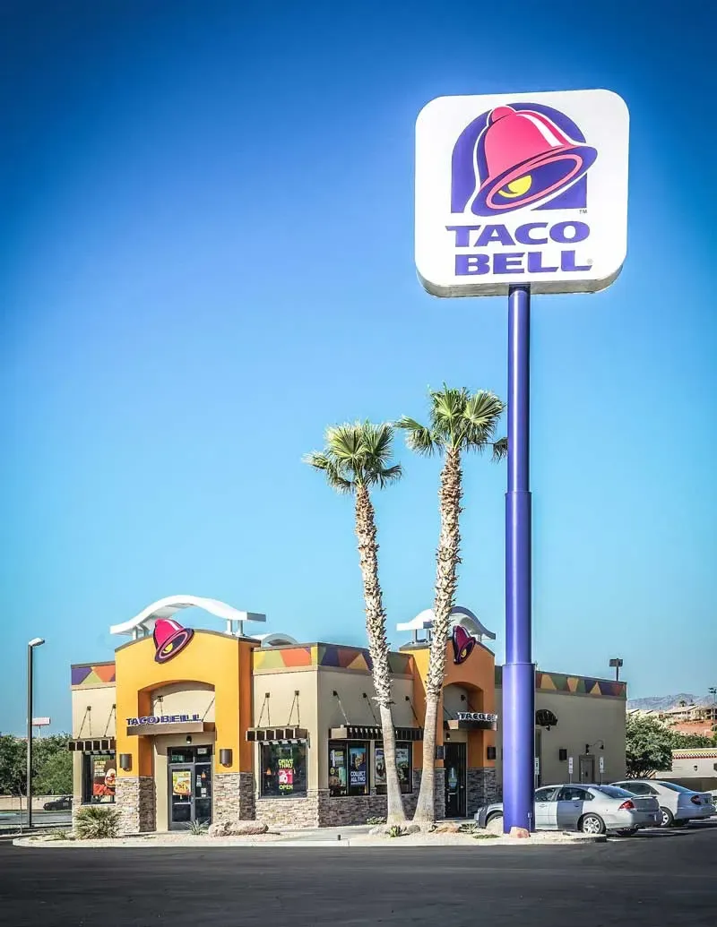 Tall Taco Bell pylon sign and palm trees in front of the restaurant under a clear blue sky