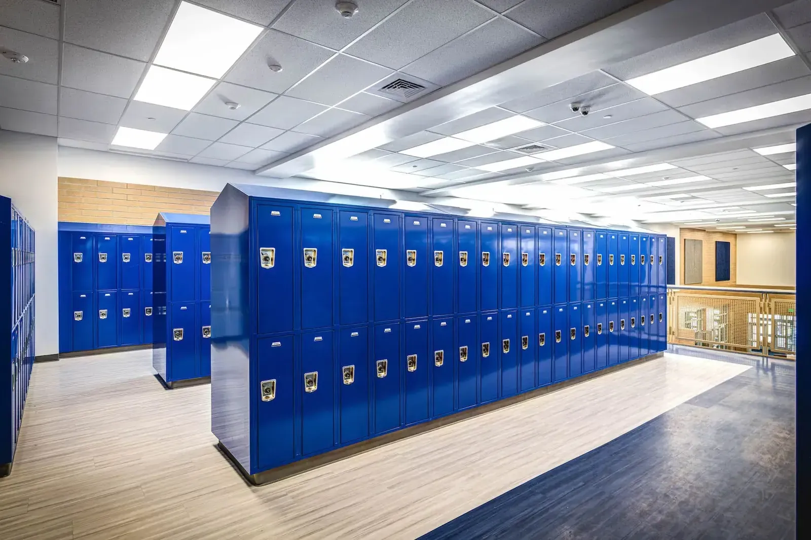 Hallway lined with blue lockers on a wood-look floor.