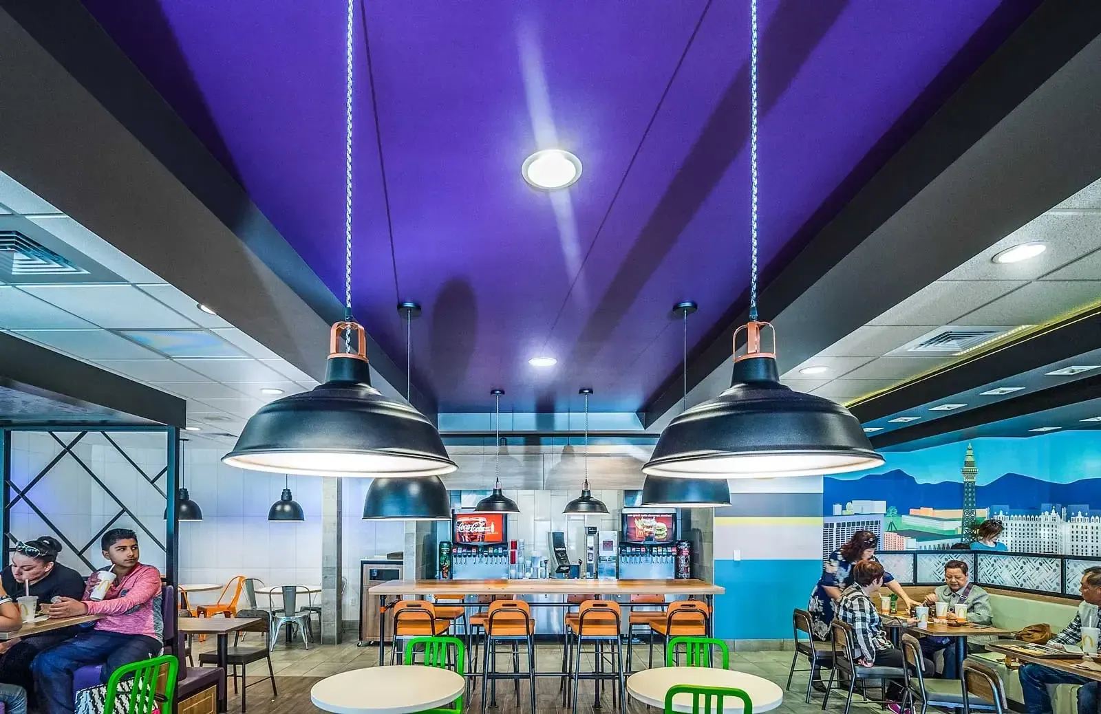 Dining room under a purple ceiling with black pendant lights and round tables.