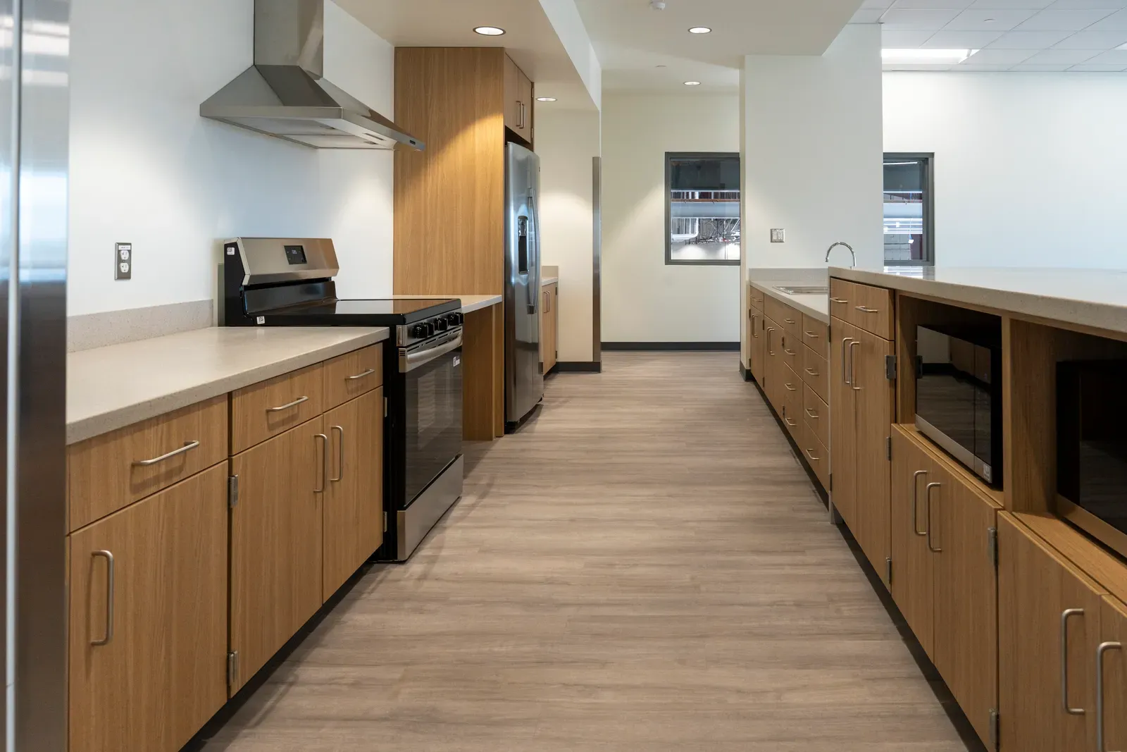 Galley kitchen with wood cabinets, a range, a refrigerator and microwaves built into the island.