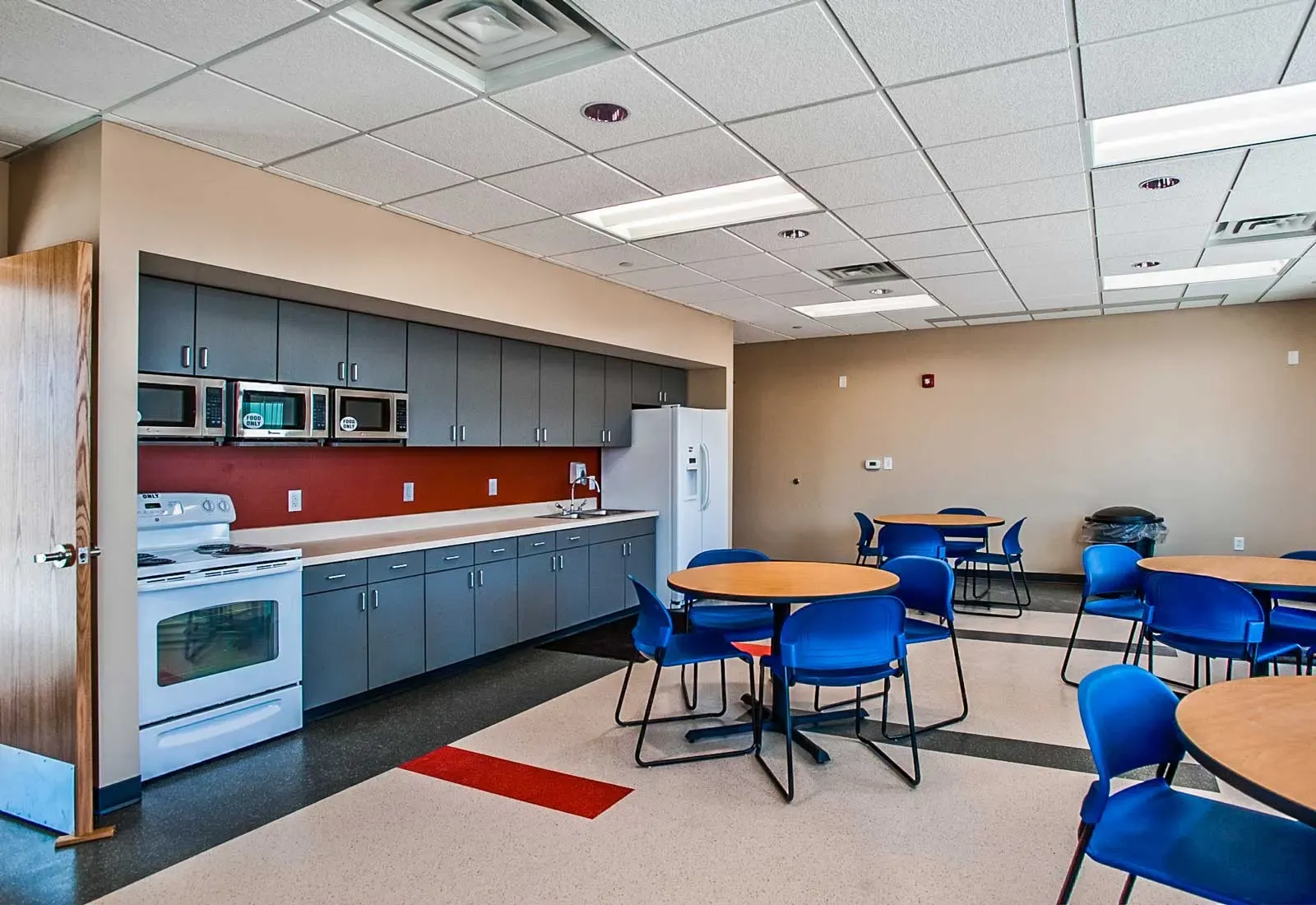 Break room with a kitchen along one wall and round tables with blue chairs