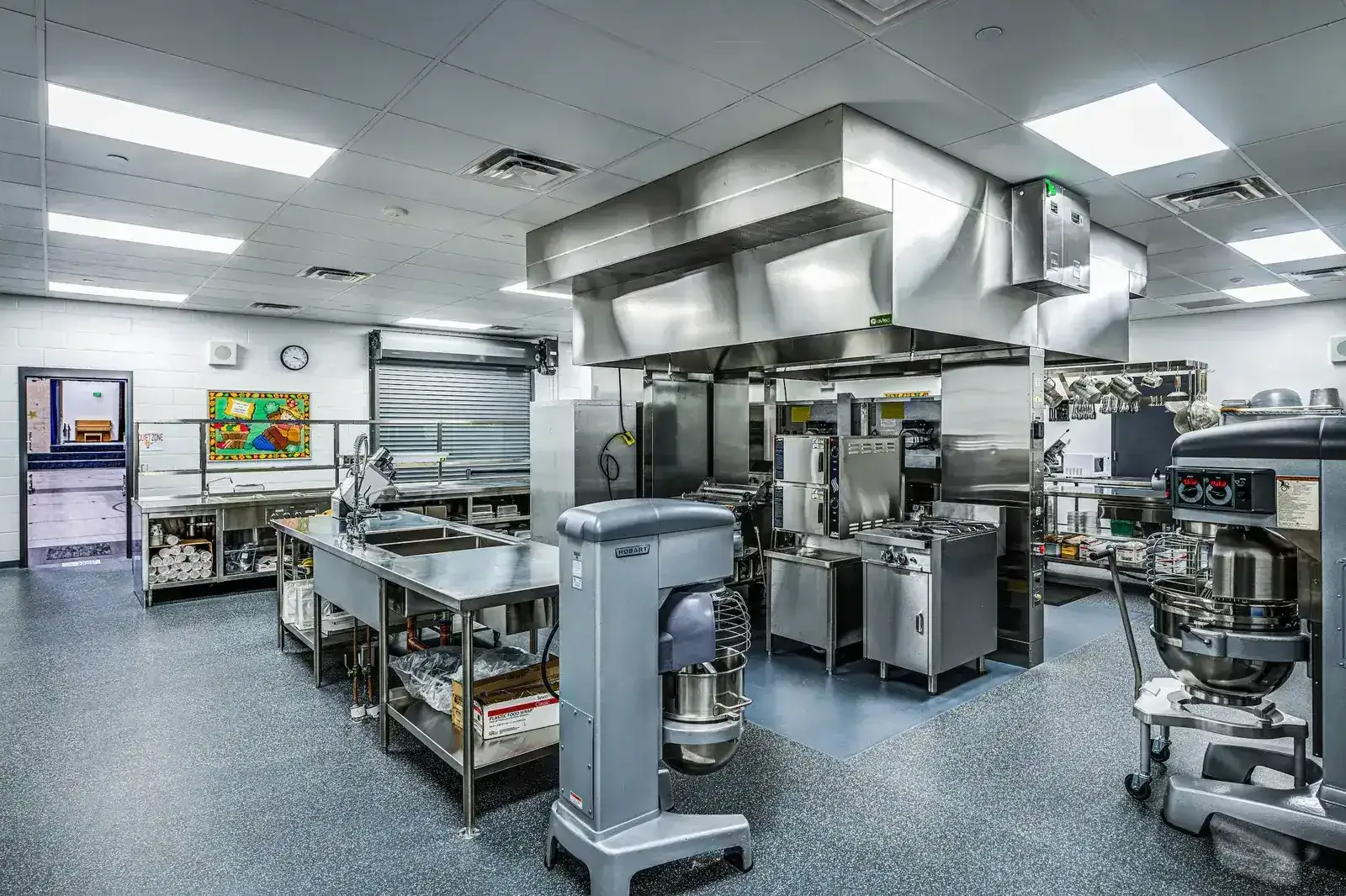 School kitchen with stainless steel equipment, a range hood and a large floor mixer.