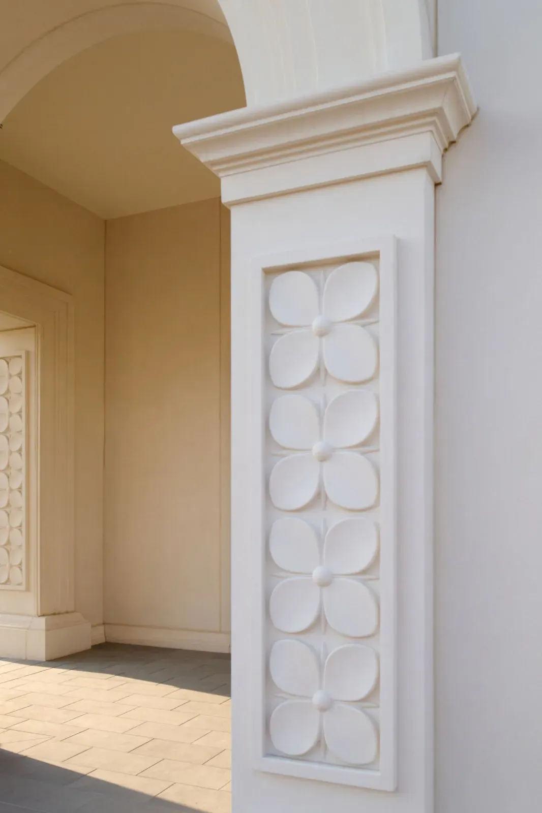 Close view of a white entrance pillar carved with a column of four-petal flower reliefs, beside an arched portico.