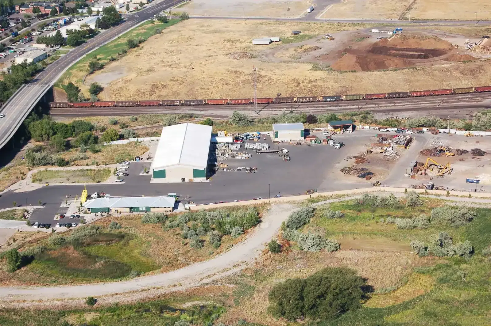Aerial view of the recycling site with buildings, a scrap yard and a rail line along the back.