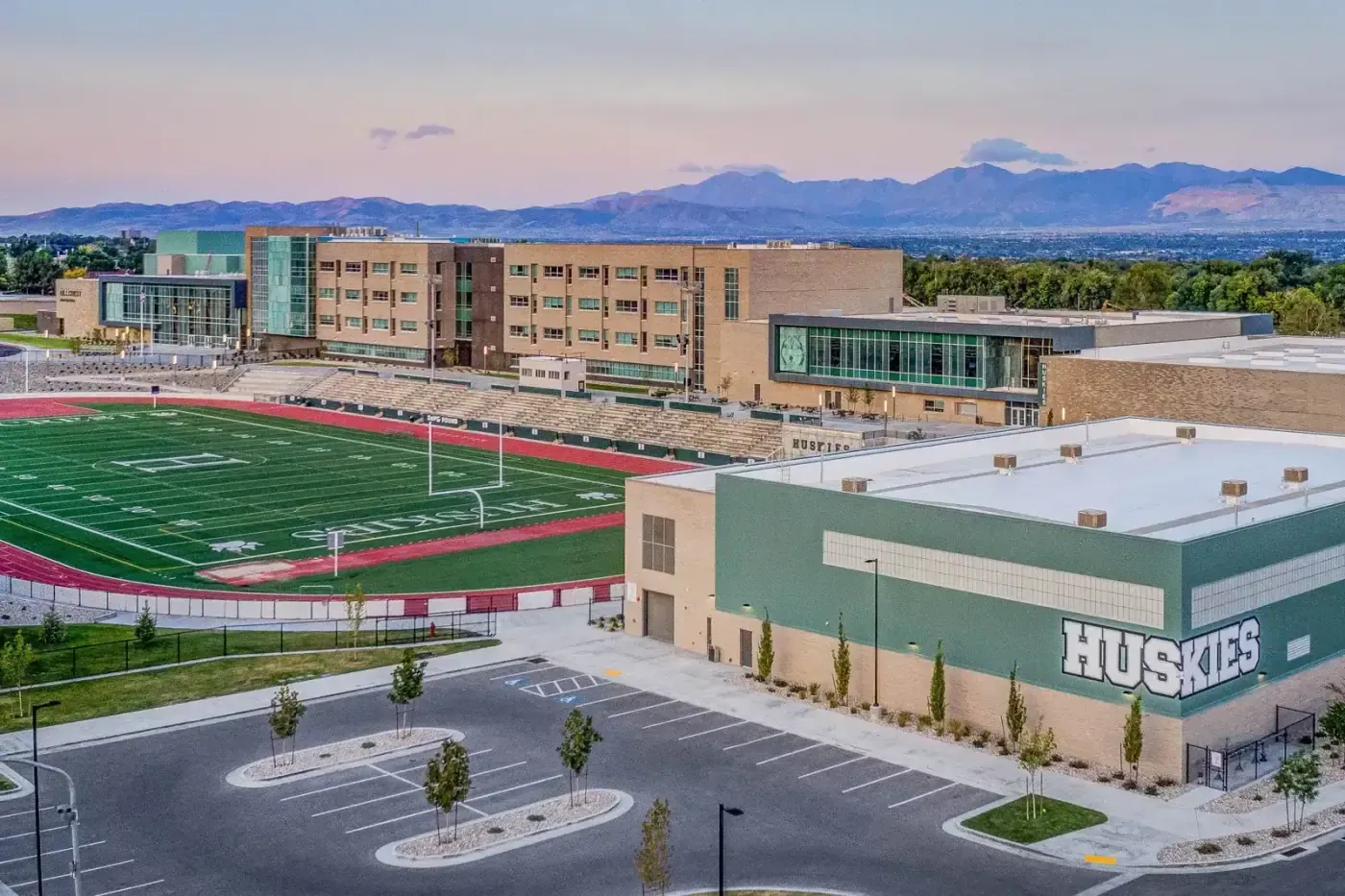 Aerial view at dusk of the school, the football field and a Huskies-lettered building with mountains beyond