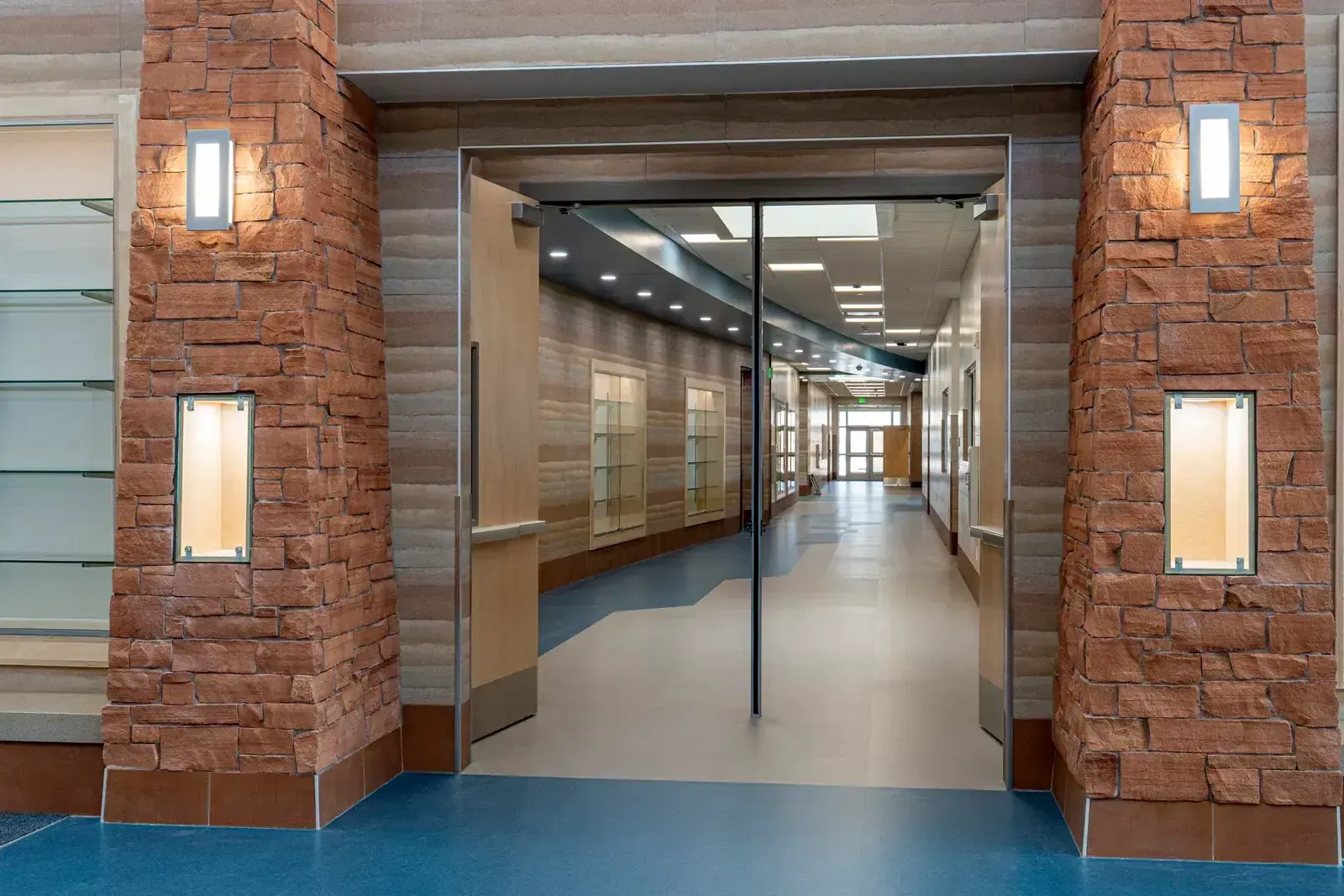 Doorway between two red stone columns opening to a curved corridor with a blue and tan floor.