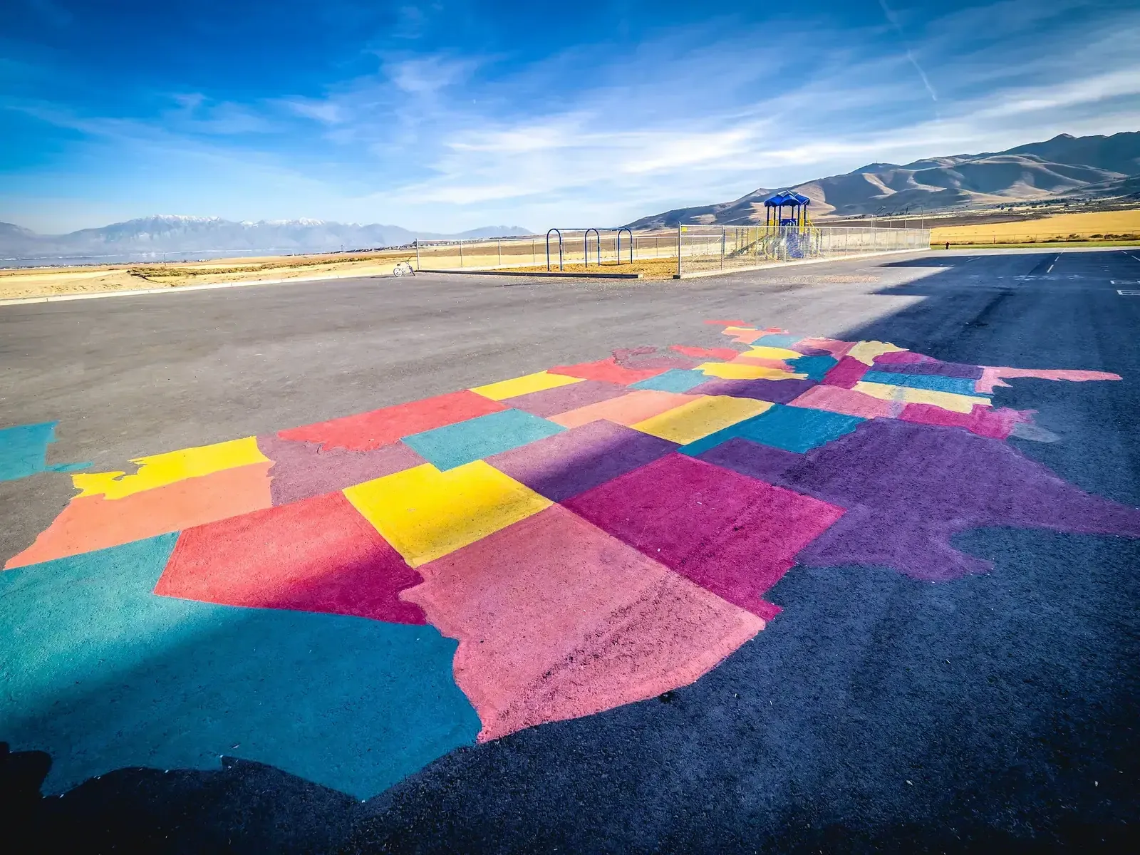 Asphalt play area painted in bright colored shapes, with a play structure and mountains in the distance