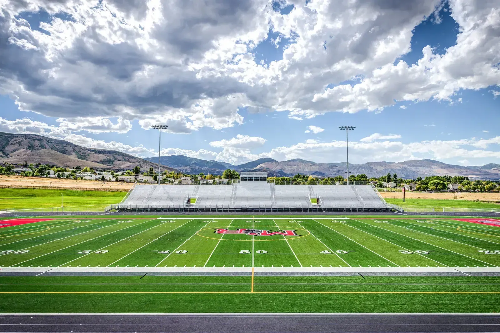 Football stadium with a turf field, grandstand and mountains beyond.