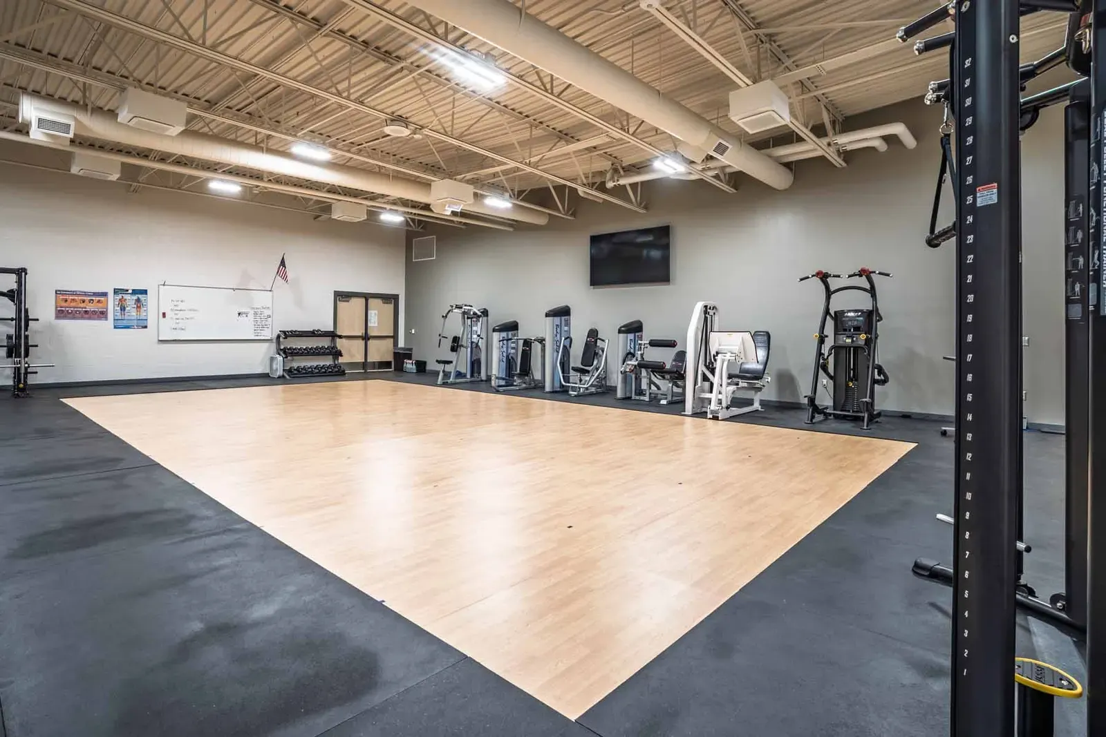 Fitness room with strength machines around an open wood-floored area.