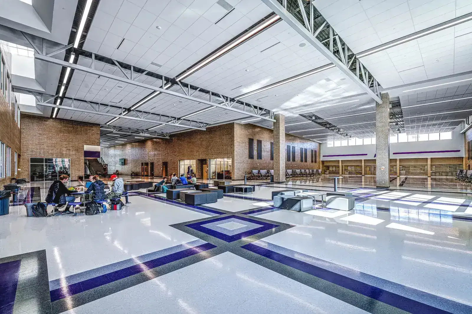 Commons with exposed steel trusses, a purple and gray tile floor and seating areas.