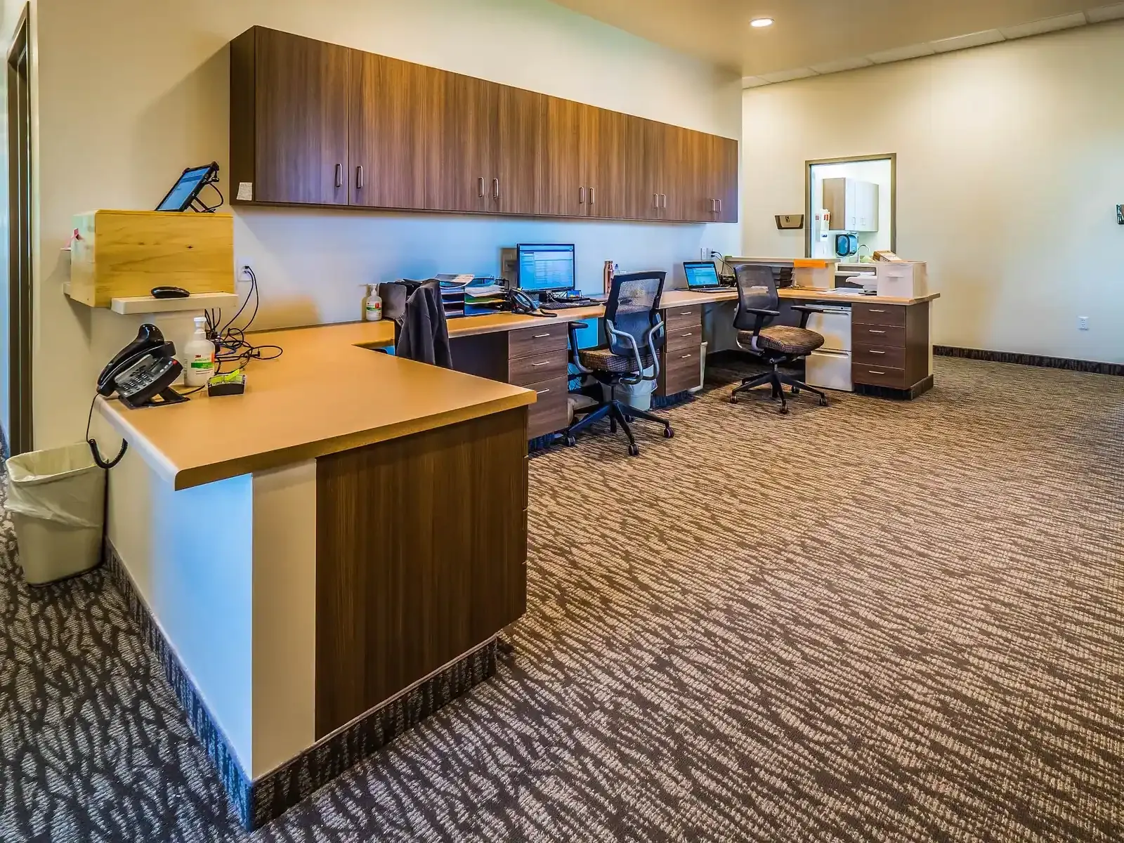 Staff work area with wood-grain desks, wall cabinets and computers.