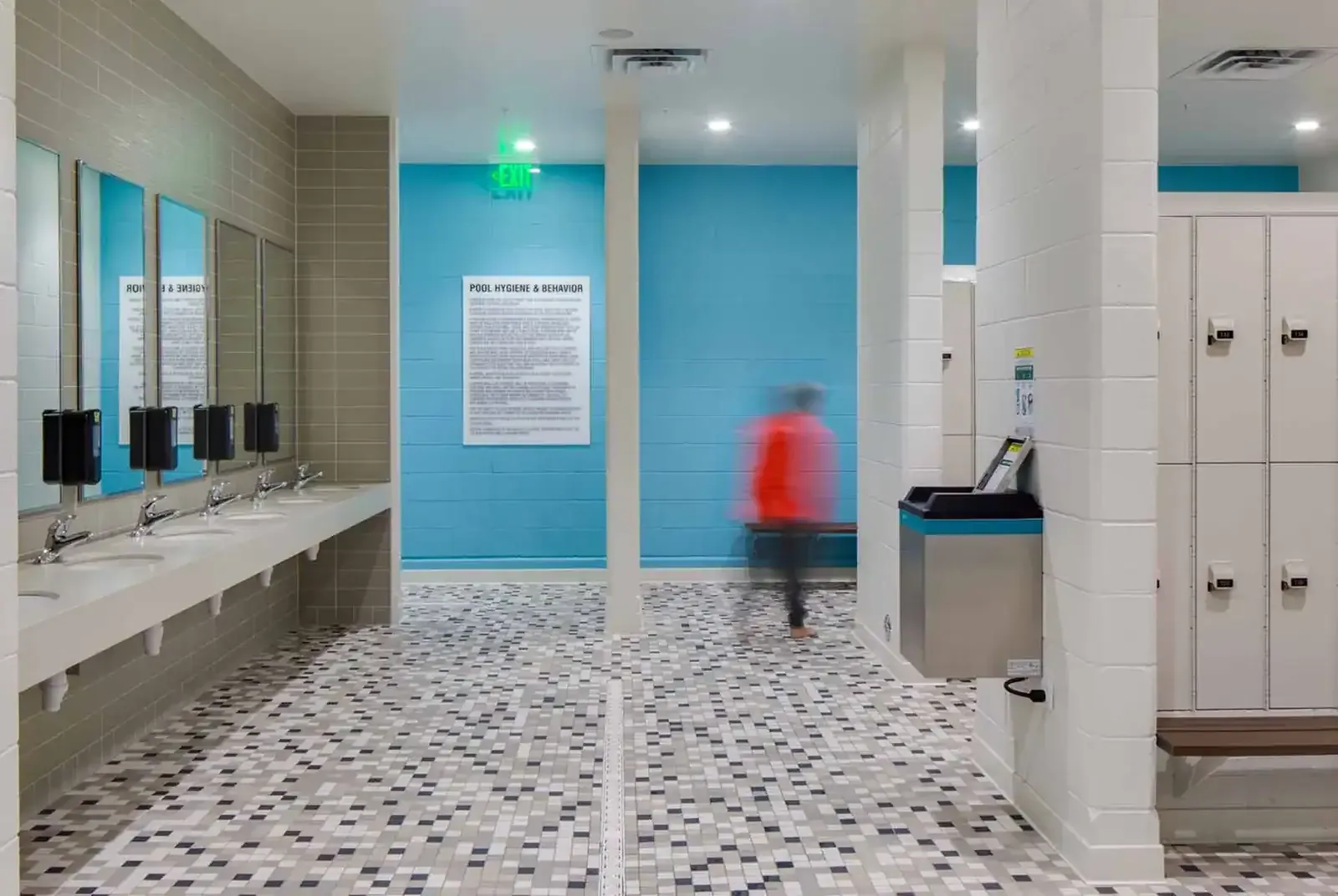 Locker room with a long sink counter, mirrors, lockers and a blue accent wall.
