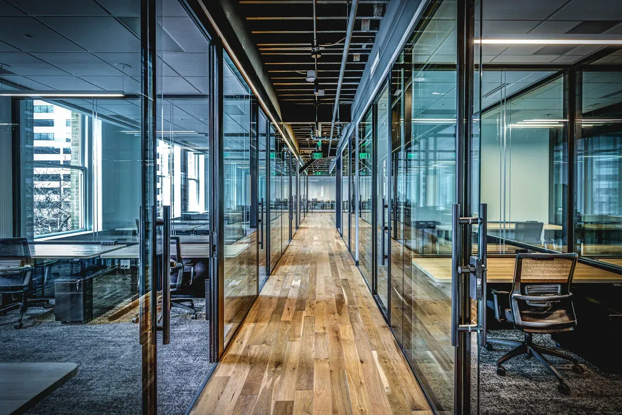 Corridor lined with glass-walled offices and a wood floor.