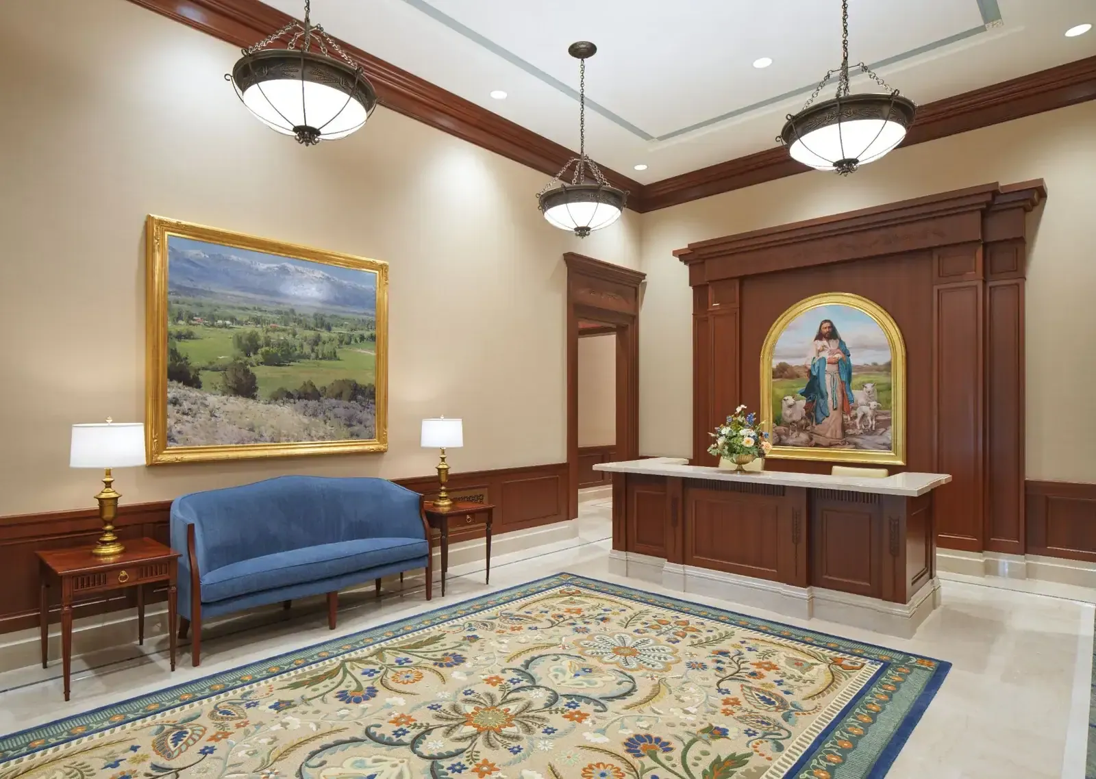 Entry area with a wood reception desk beneath a framed painting, a blue settee, a large landscape painting and a patterned rug