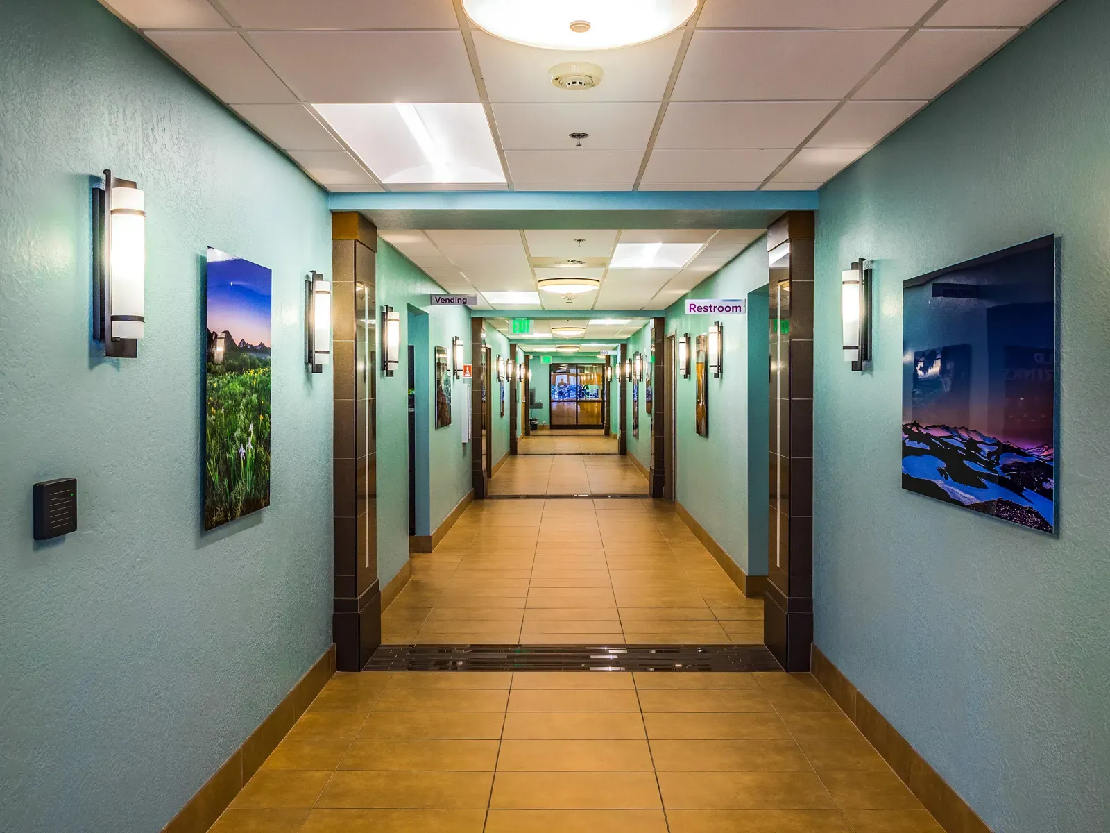 Corridor with tile floor and teal walls, with framed landscape photographs on both sides.