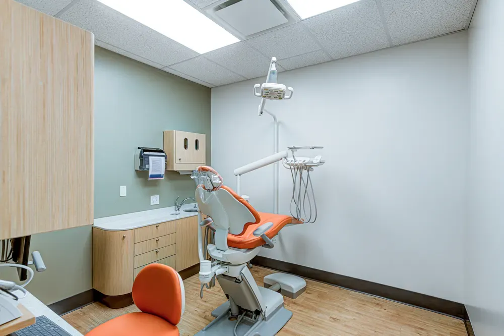 Dental exam room with an orange dental chair and wood cabinets.