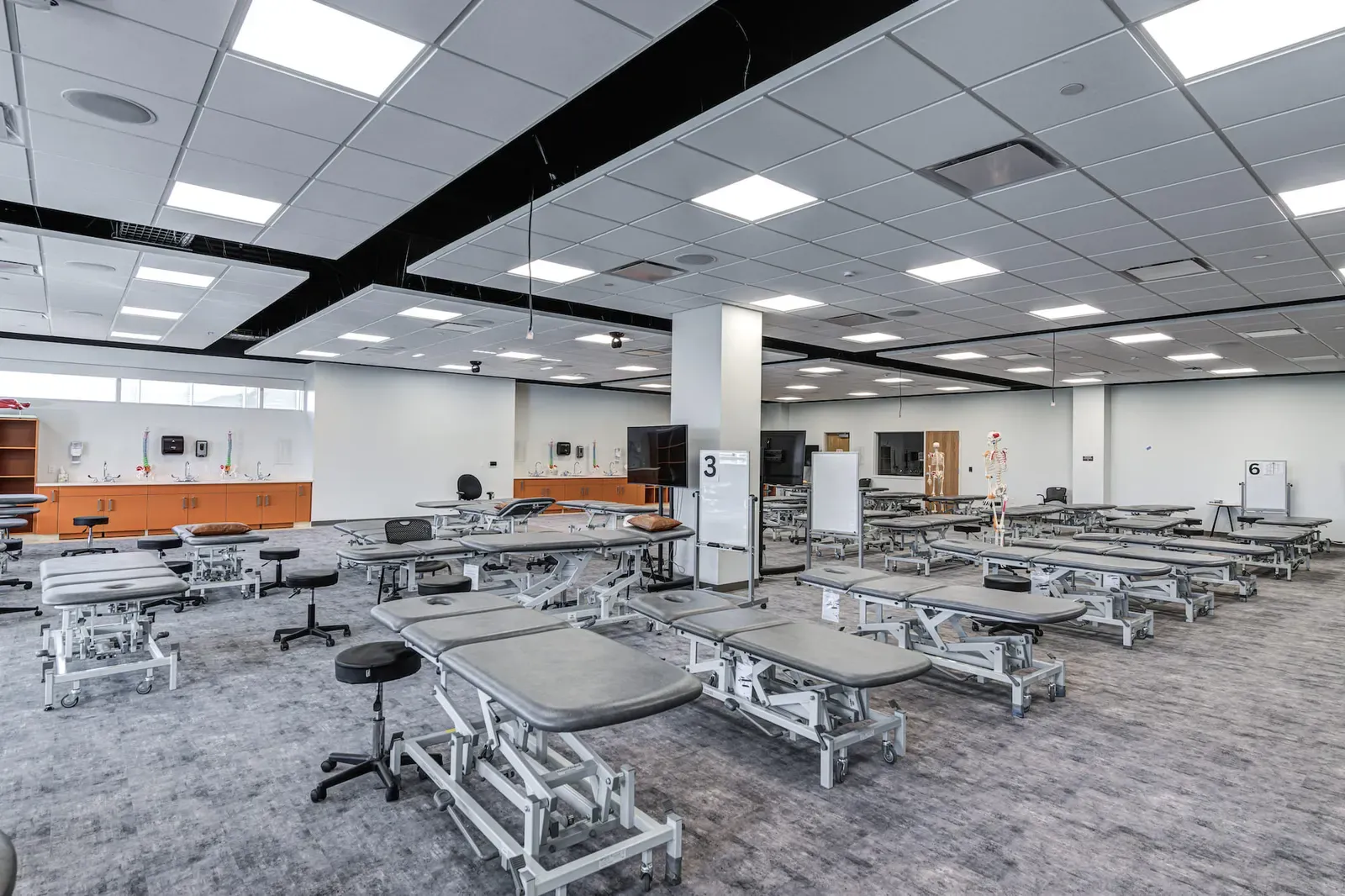 Skills lab with rows of padded treatment tables and wall-mounted displays.