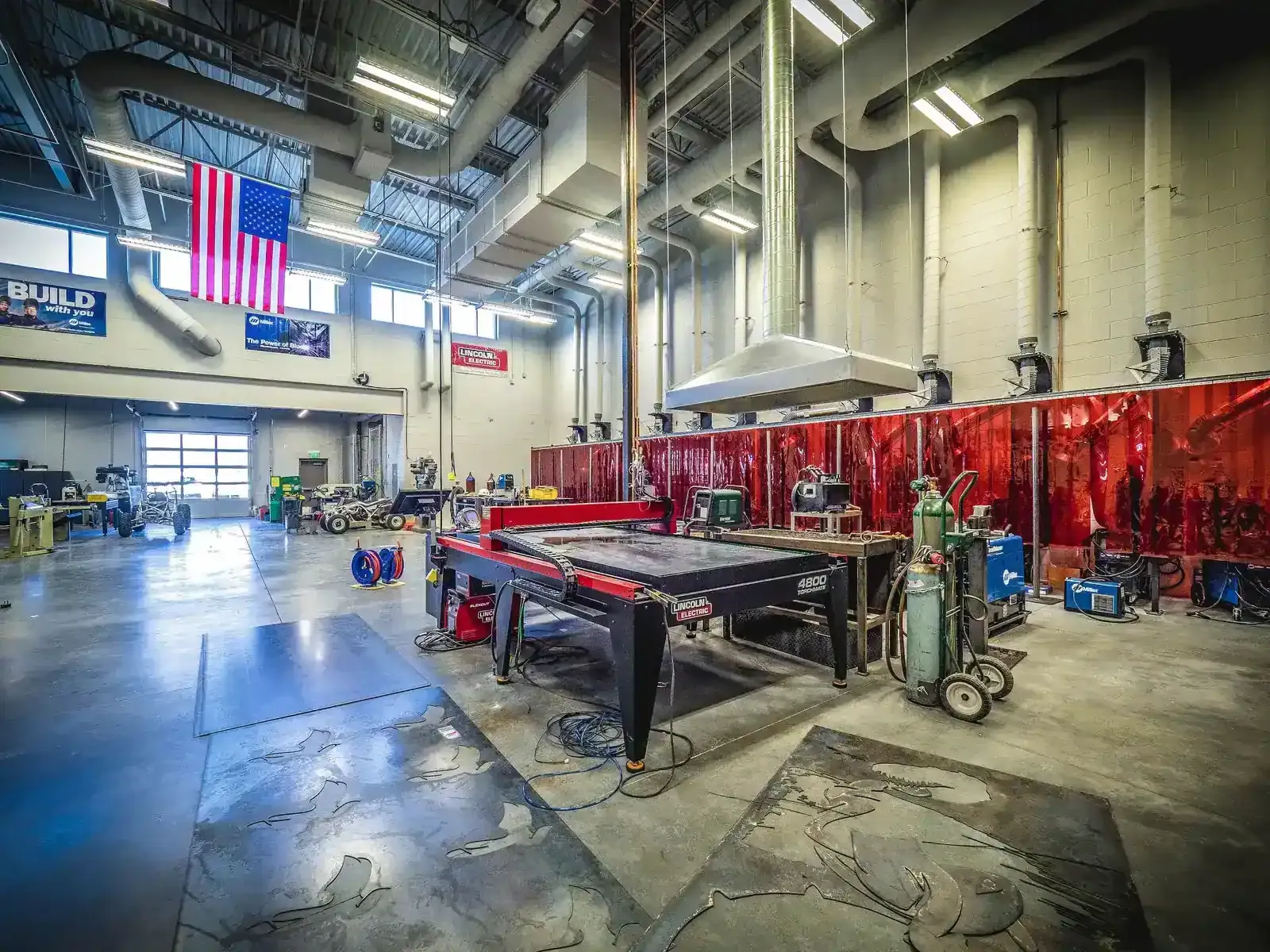 Metal fabrication shop with a CNC plasma cutting table, gas cylinders and a red welding curtain