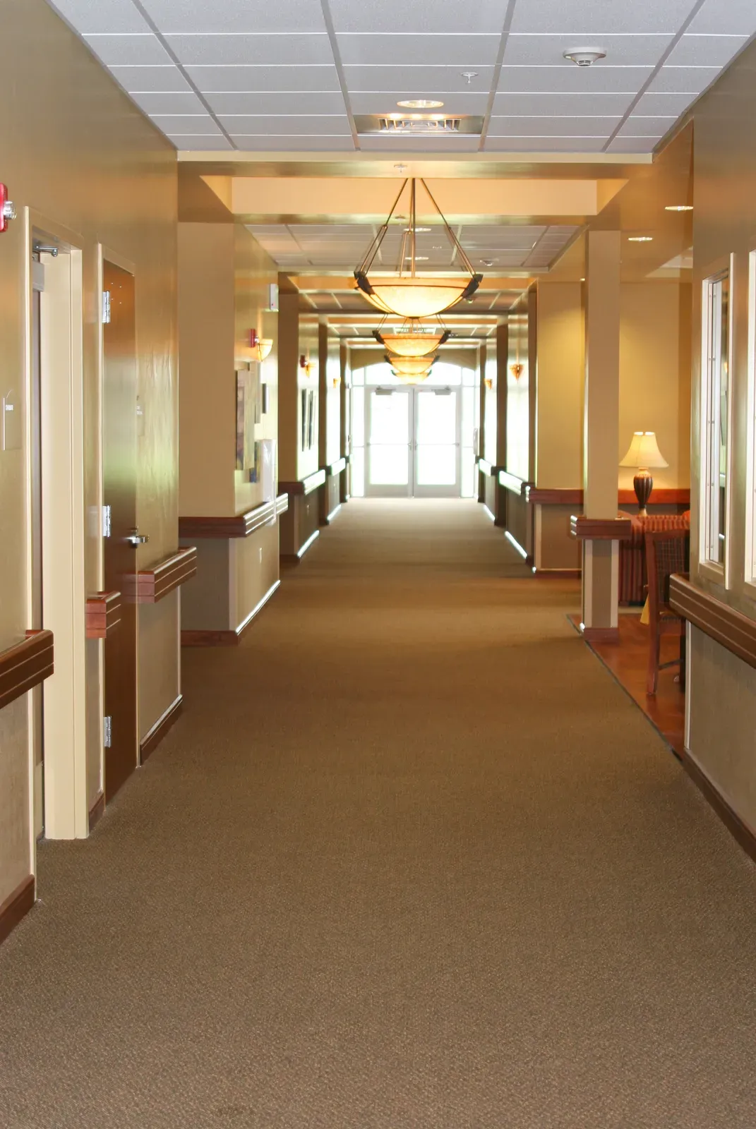 Long carpeted corridor with handrails and pendant lights leading to glass doors.