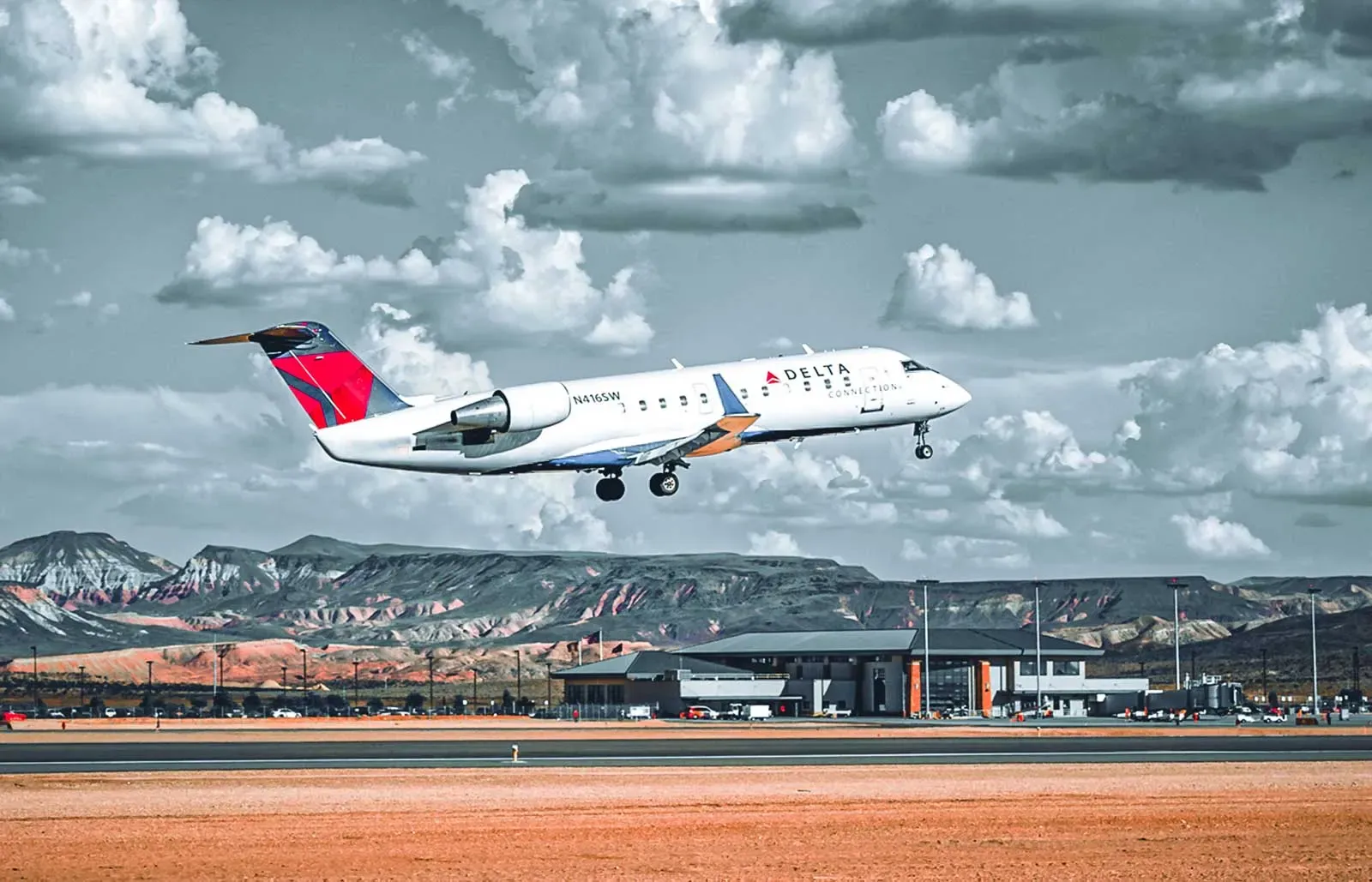 Regional jet lifting off the runway, with the terminal building and red-rock mountains in the distance.