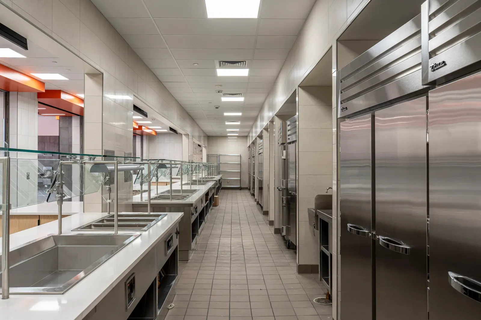 Service line with stainless steel counters, glass sneeze guards and tall stainless refrigerators.