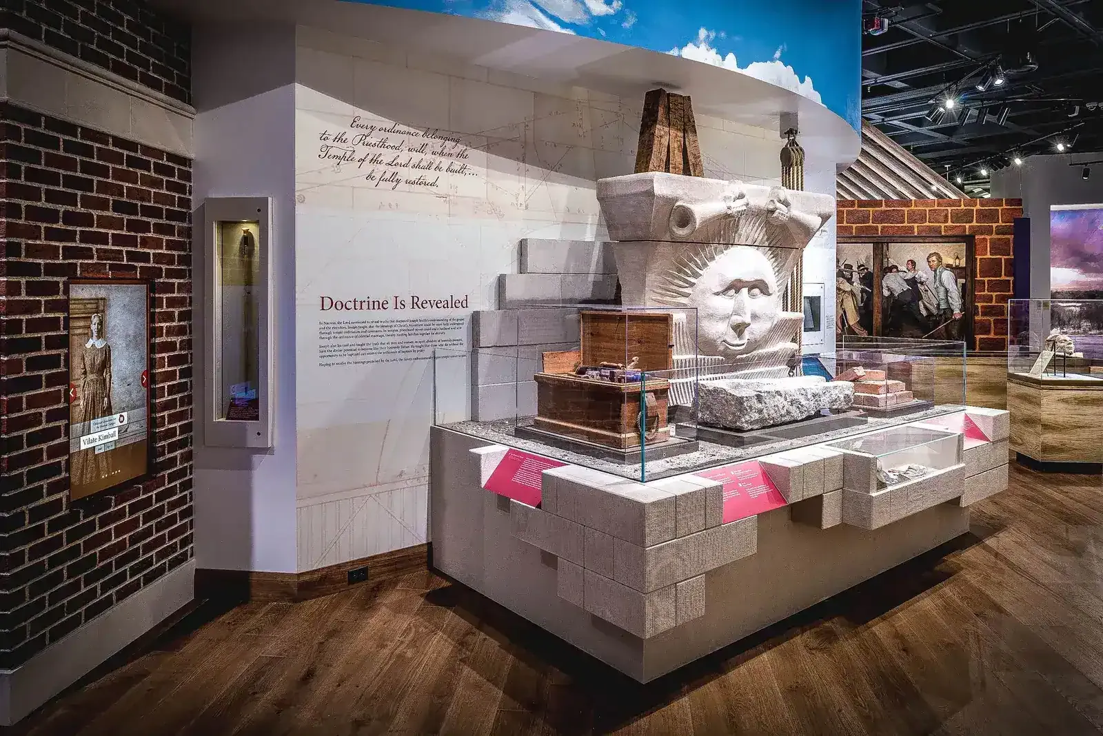Exhibit with a carved stone sunburst face and artifact cases on a stone-block platform
