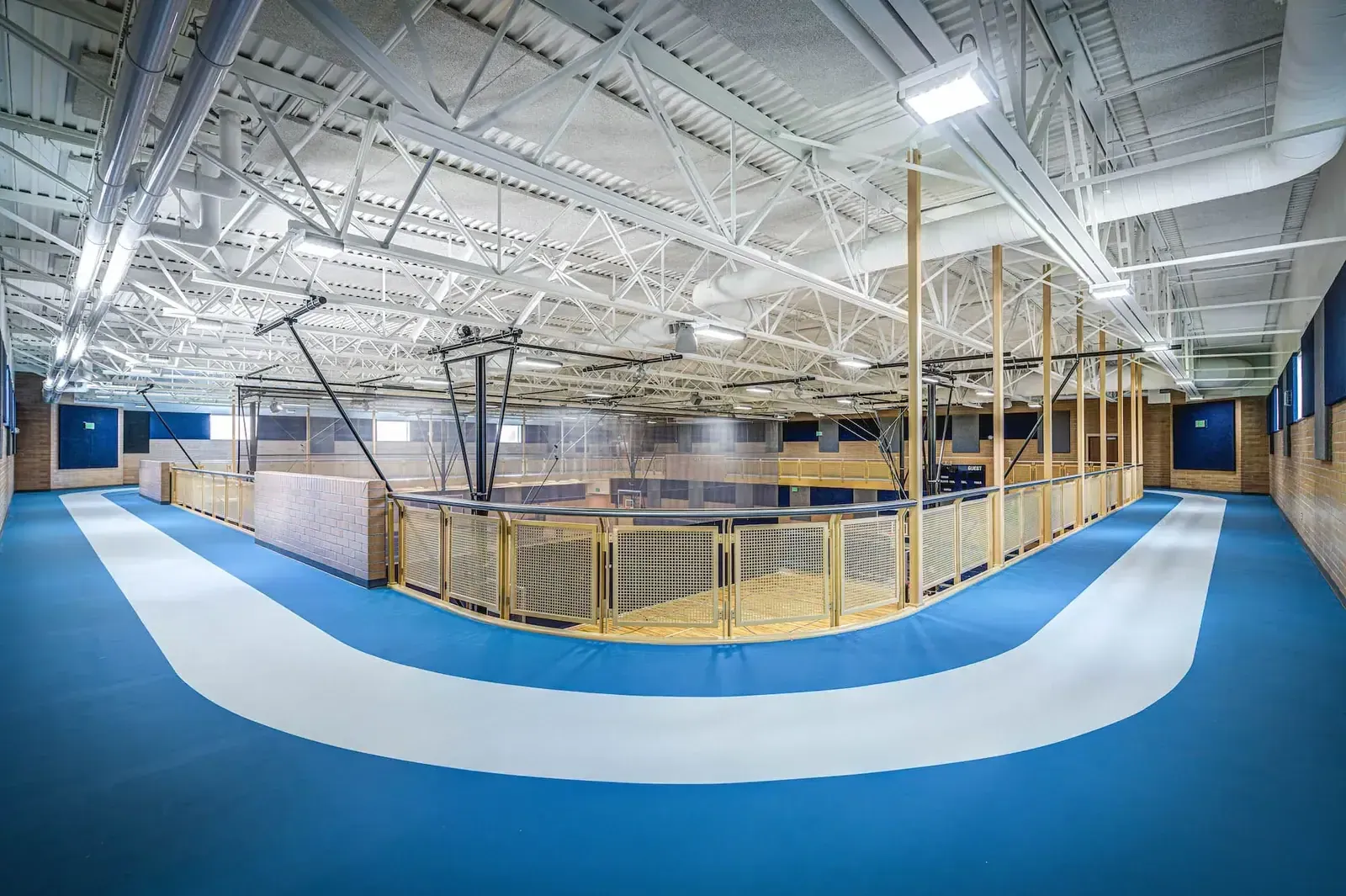 Blue and white indoor running track curving around the gym under a steel-truss ceiling.