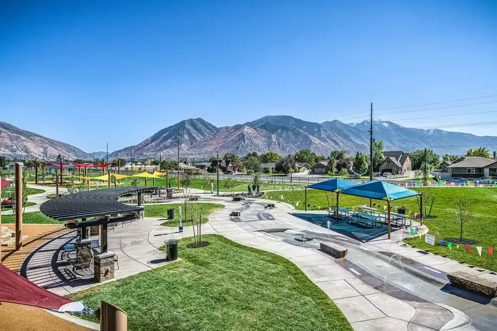 Wide view of the park's paths, shade structures and splash pad with mountains in the background