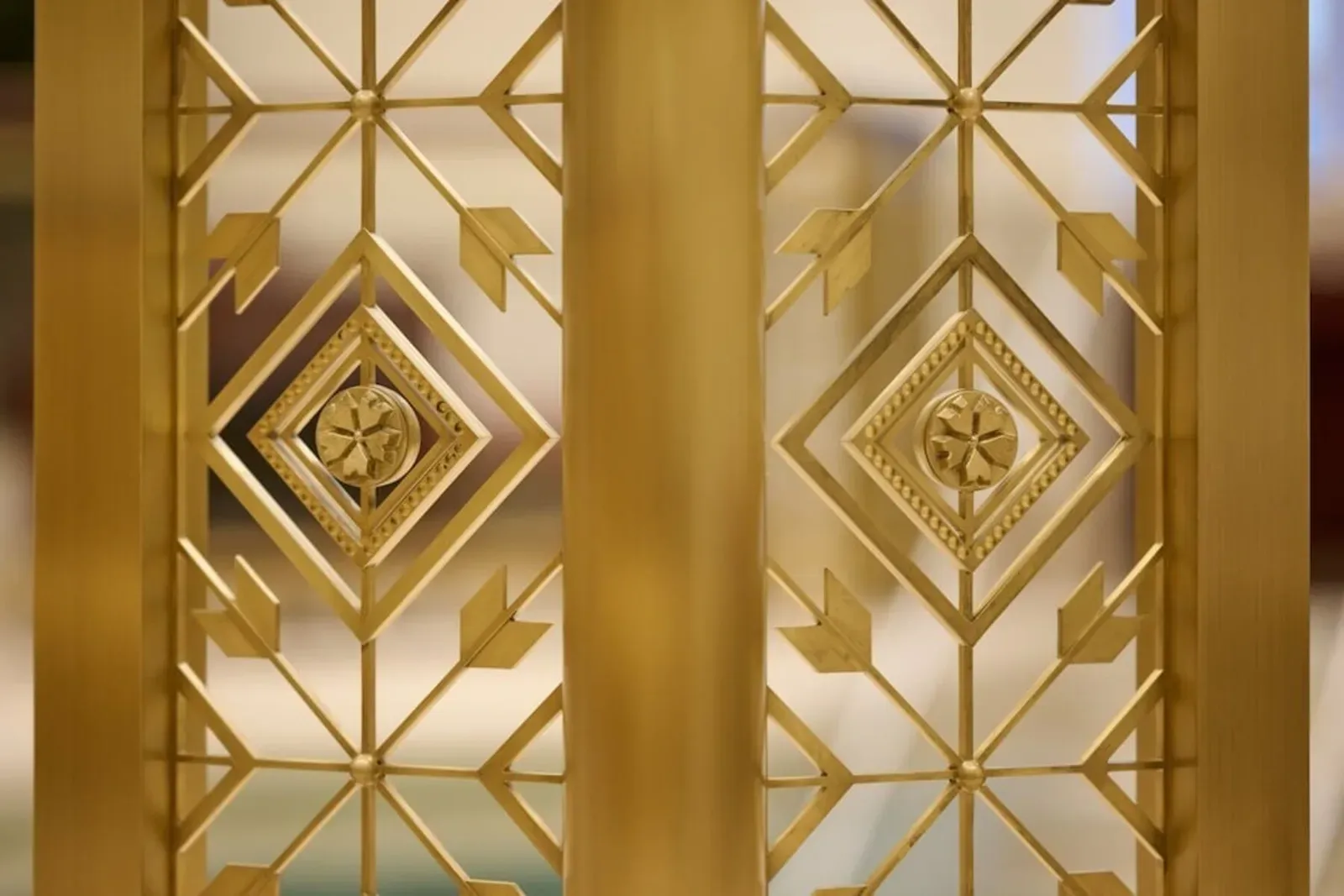 Close view of a brass screen with diamond and arrow patterns and a small flower medallion in each diamond