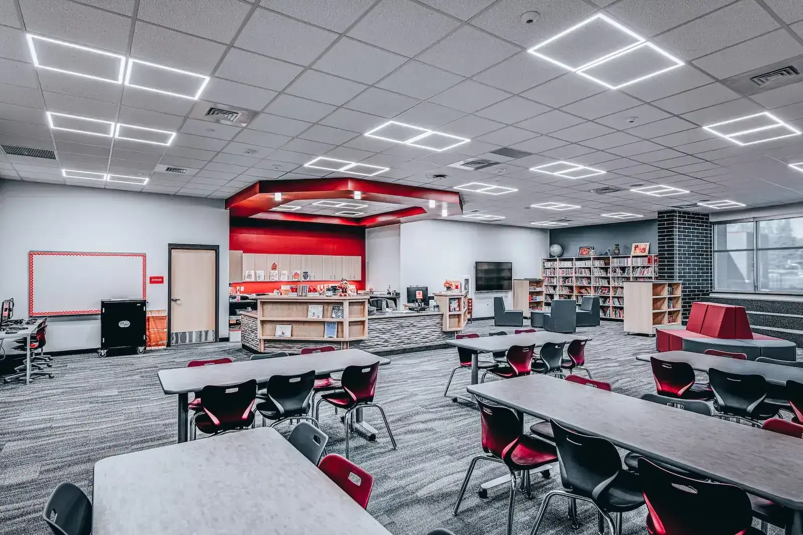 Media center with low shelving, a circulation desk, red accents and classroom tables