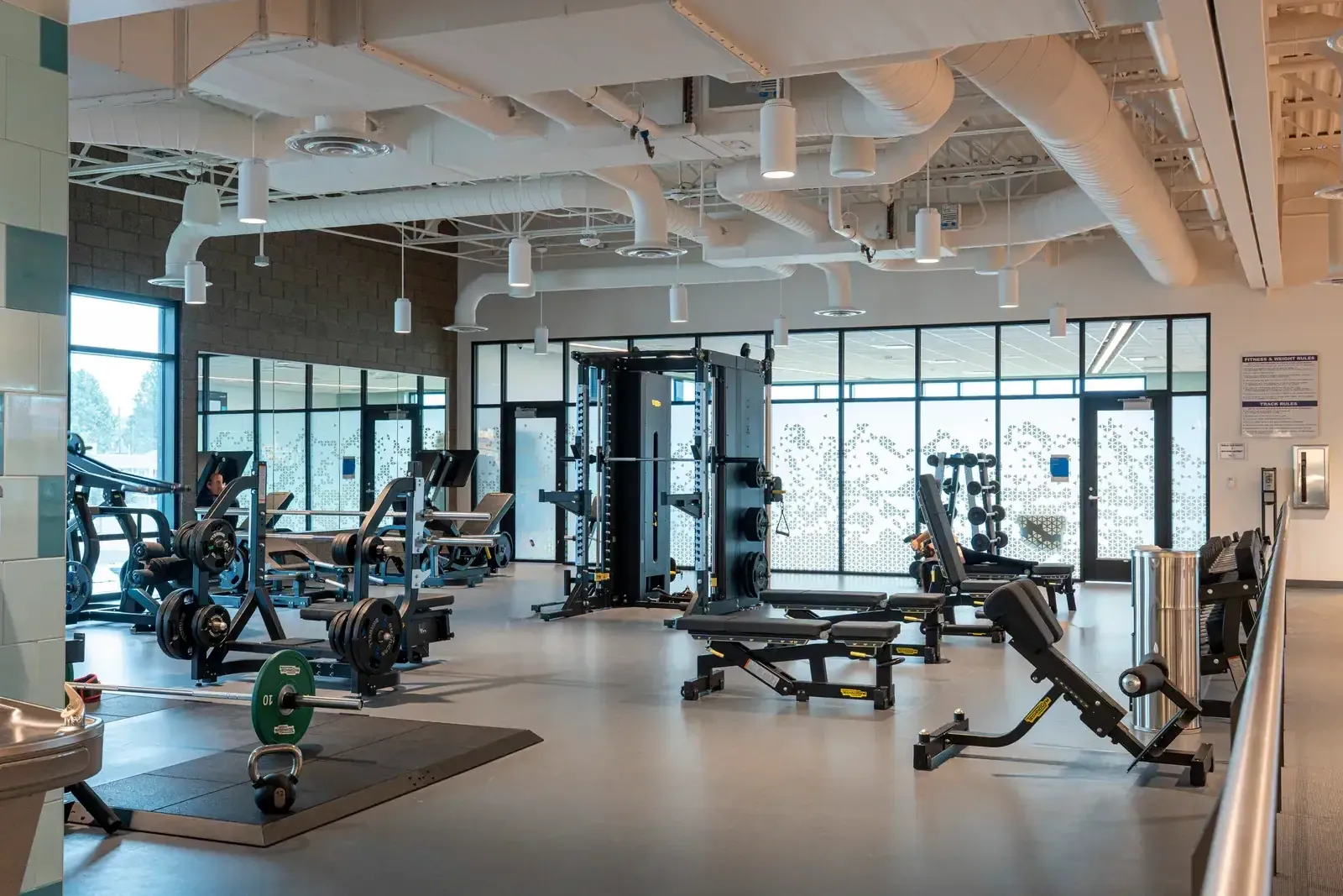 Weight area with benches, a cable machine and free weights, with patterned frosted glass doors in the background.