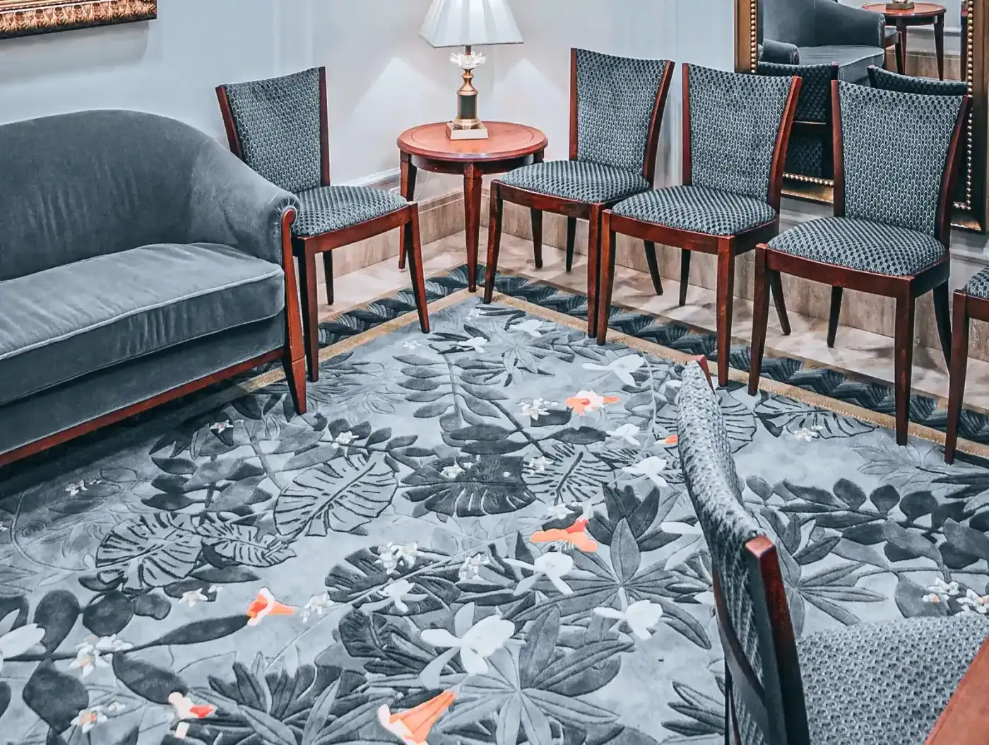 Gray-blue sofa and wood-framed chairs on a rug patterned with tropical leaves and flowers.